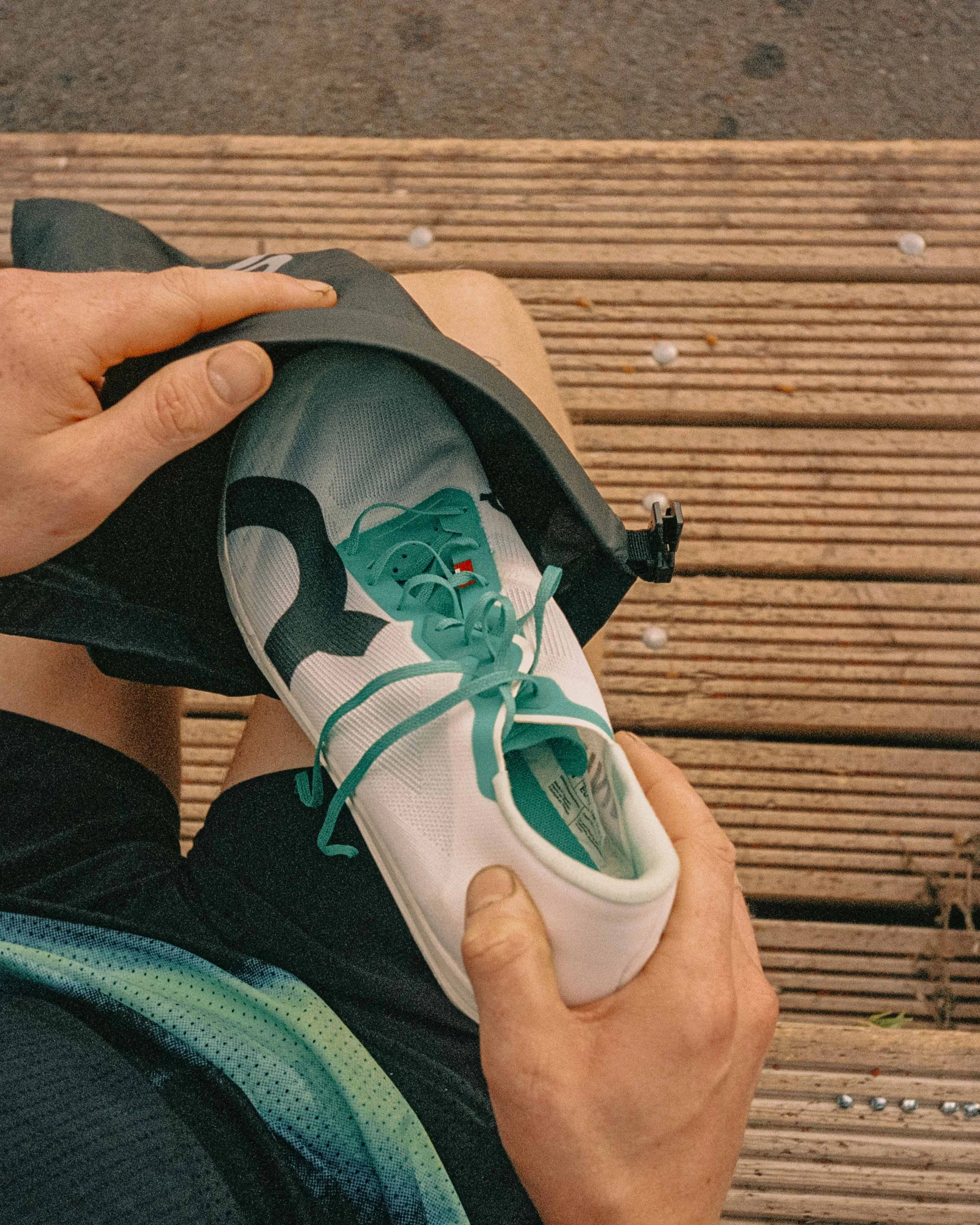 Person holding a running shoe while sitting on a wooden bench.
