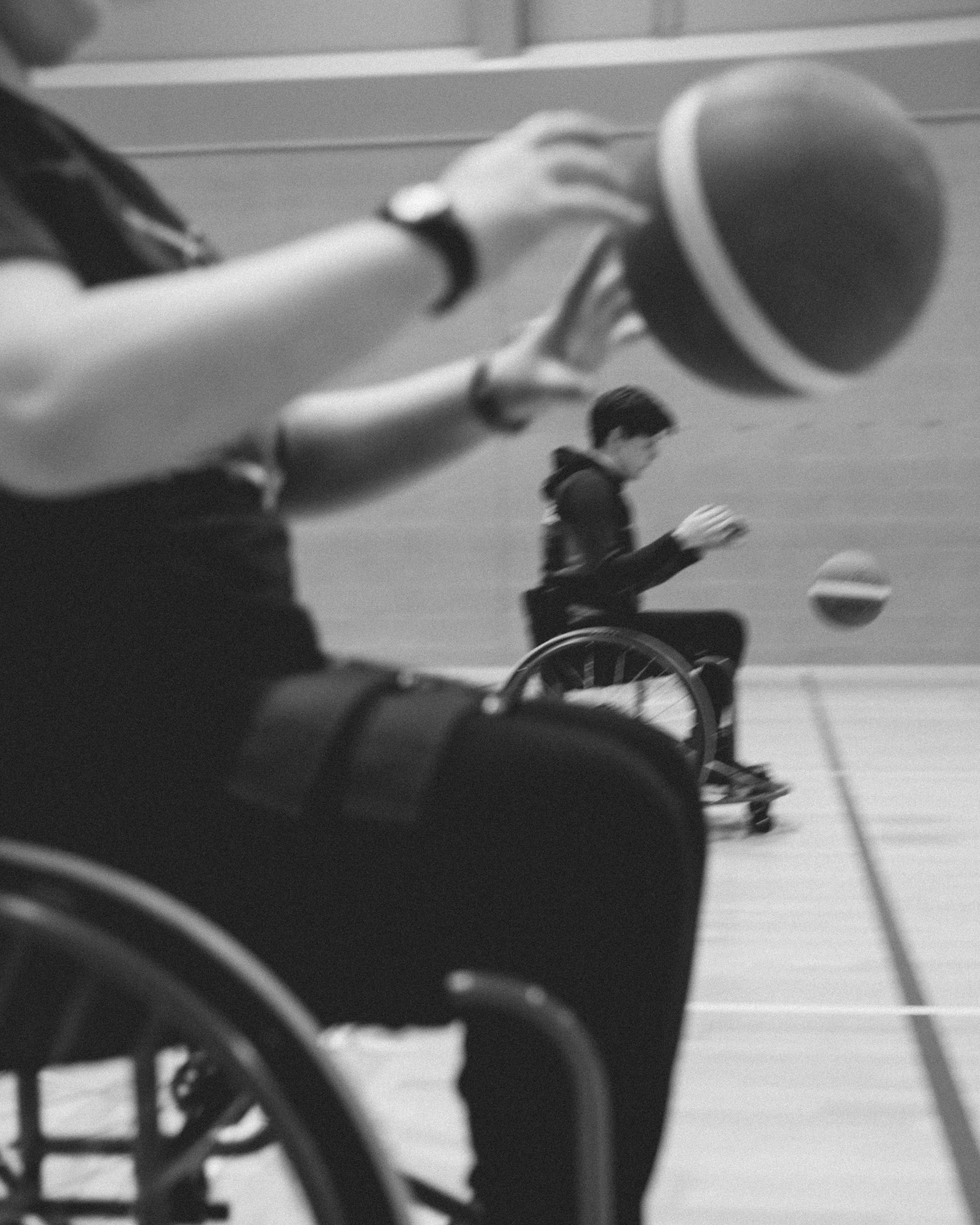 A person in a wheelchair playing with a ball in an indoor sports facility, with a coach or a trainer holding a basketball nearby.