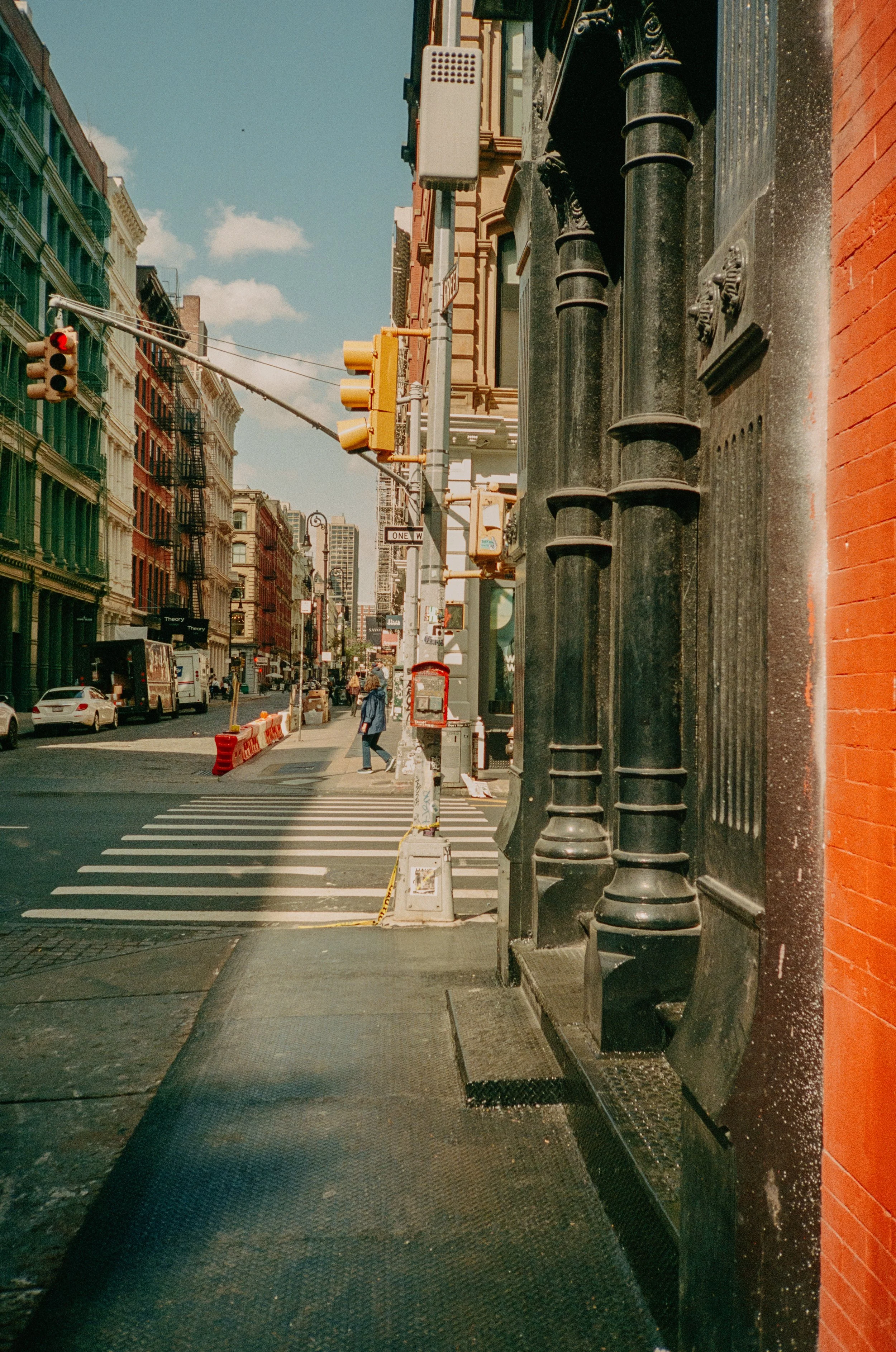 City street with buildings, traffic light, and crosswalk, taken from sidewalk with ornate black lamppost in foreground.