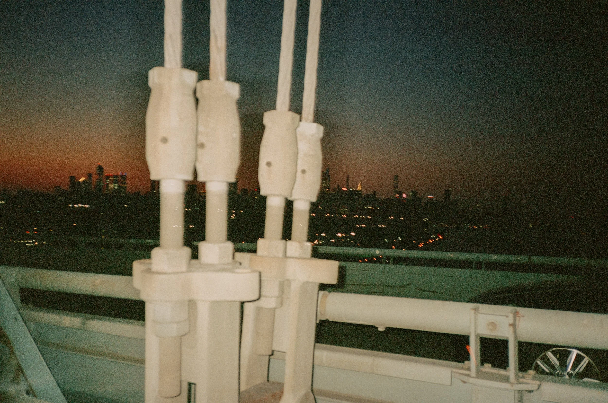 Nighttime city skyline view with illuminated buildings in the distance, viewed from a rooftop, with electrical insulators in the foreground.
