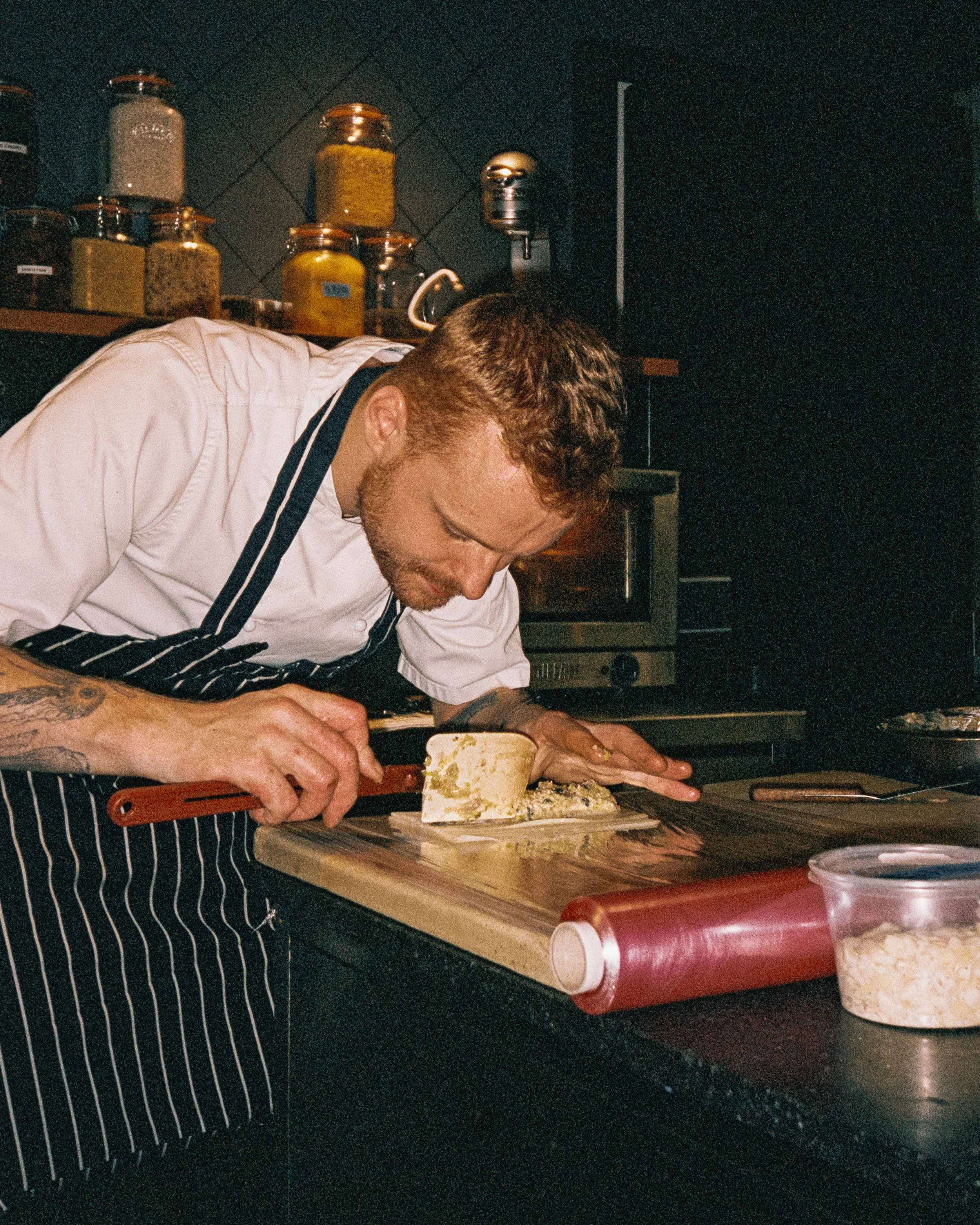 Chef slicing cheese on a wooden cutting board in a professional kitchen.
