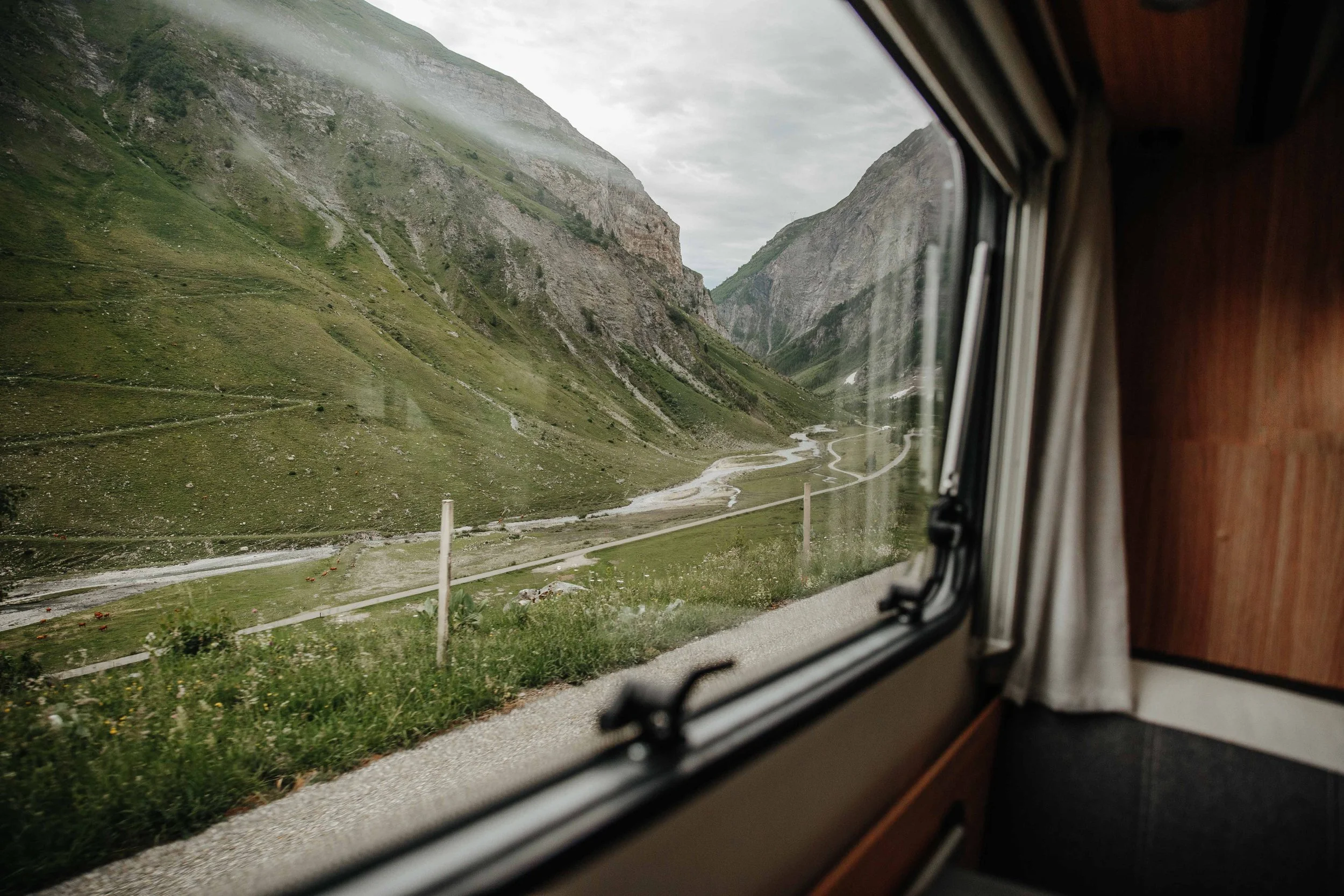 Scenic view of green mountains and a winding river seen through a bus window.