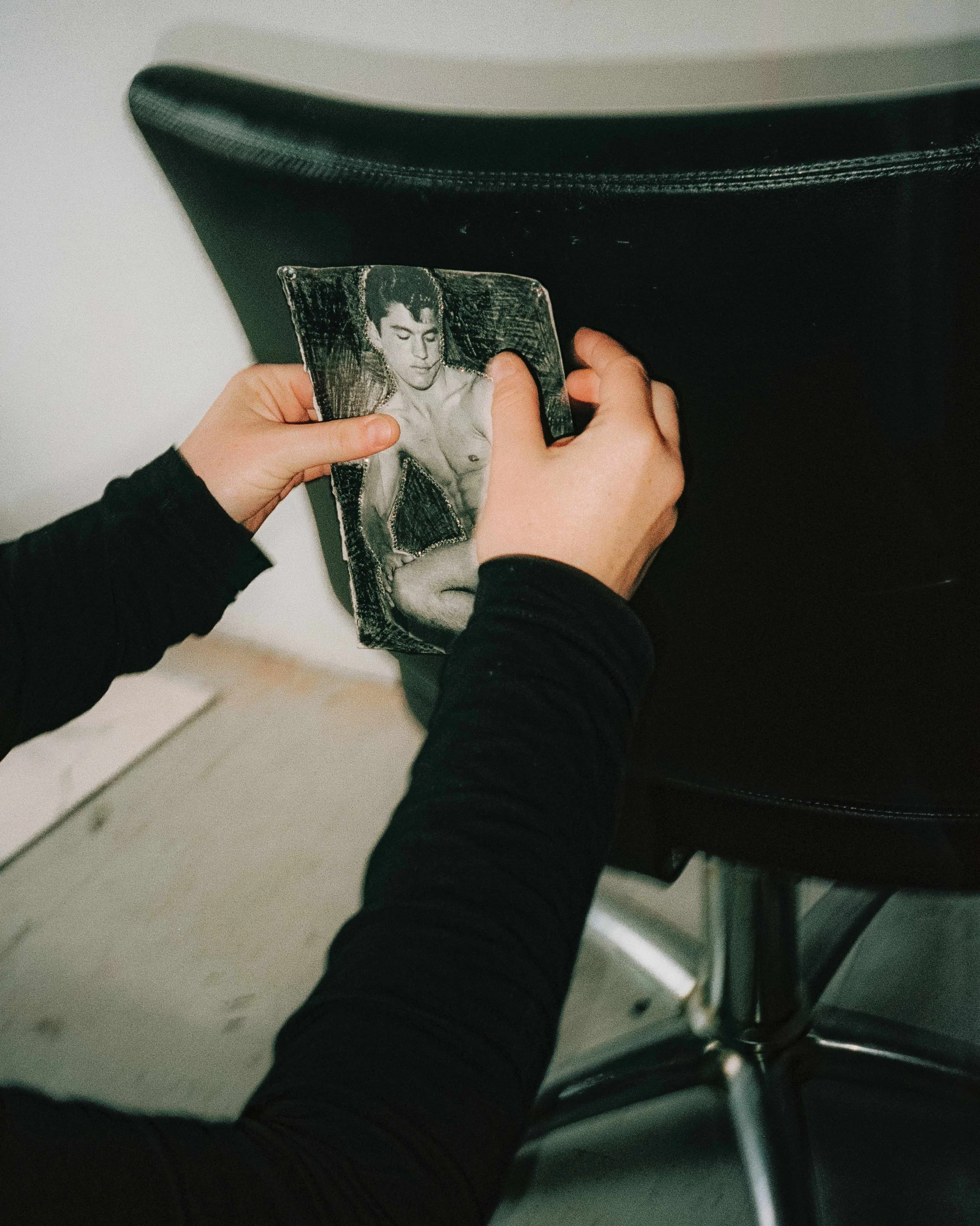 Person placing a black-and-white photo of a shirtless man into a black bag or storage container.