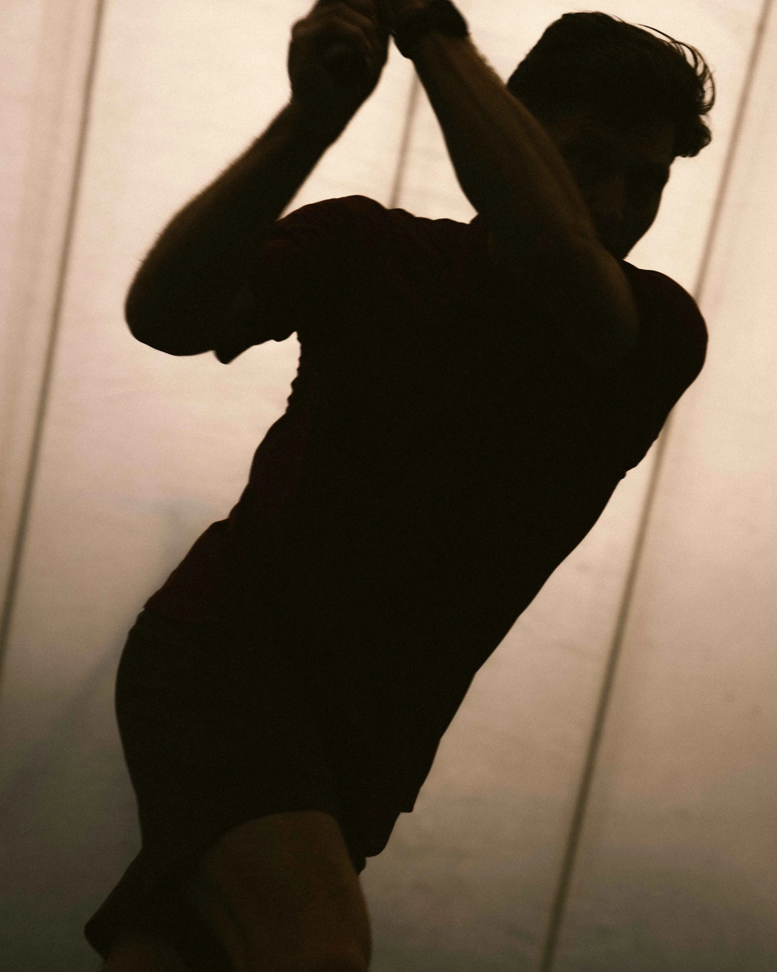 Silhouette of a person with short hair, standing and holding something above their head in front of a light-colored wall.