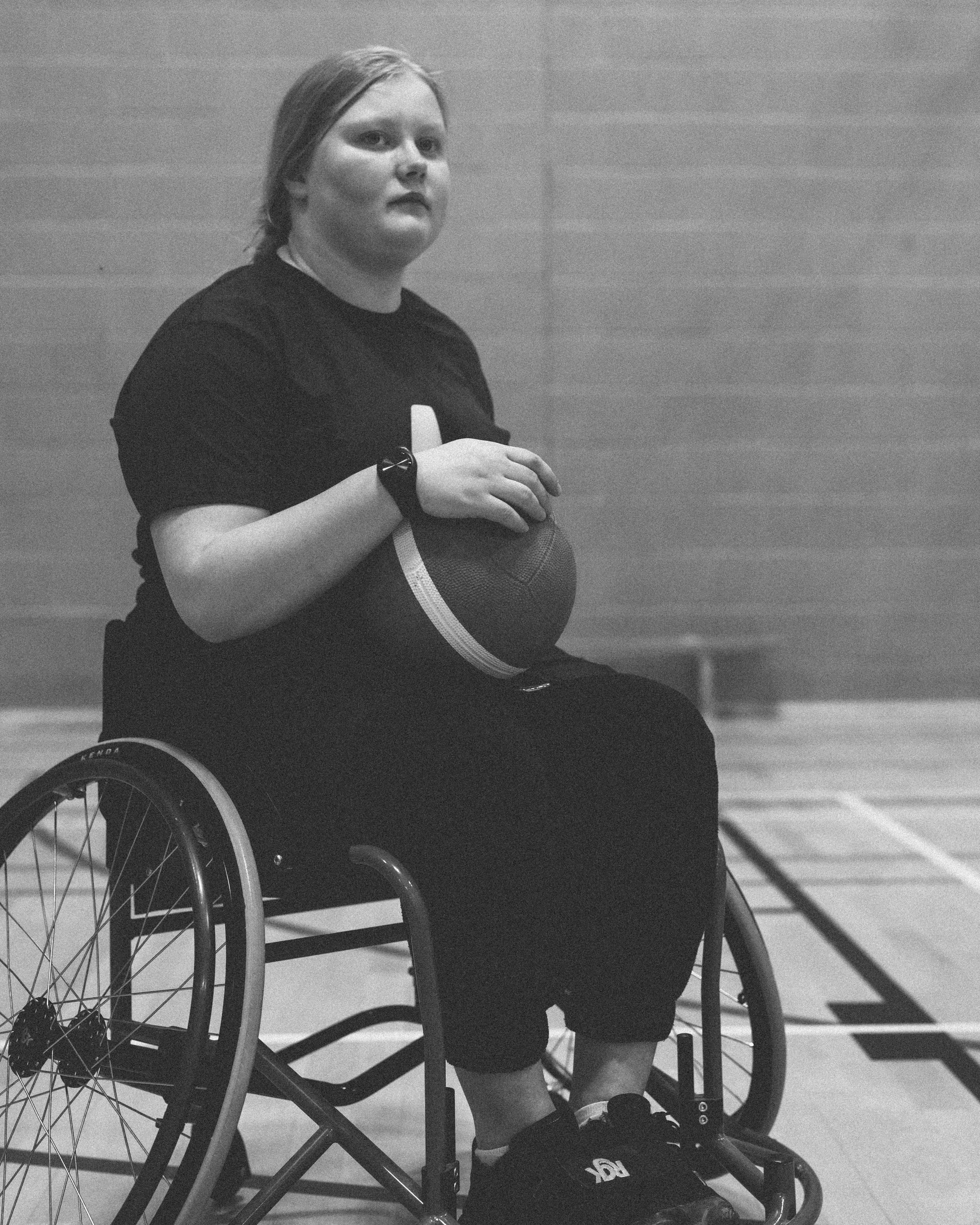 A woman in a wheelchair holding a basketball on a gymnasium court.