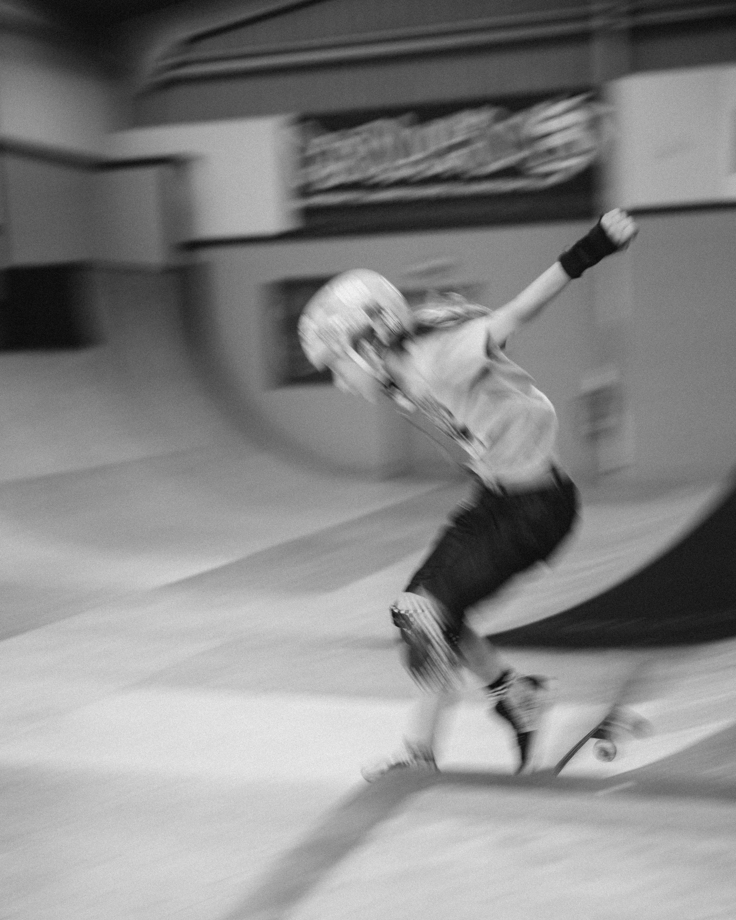 A young person wearing a helmet and protective gear skating on a ramp in a skatepark.