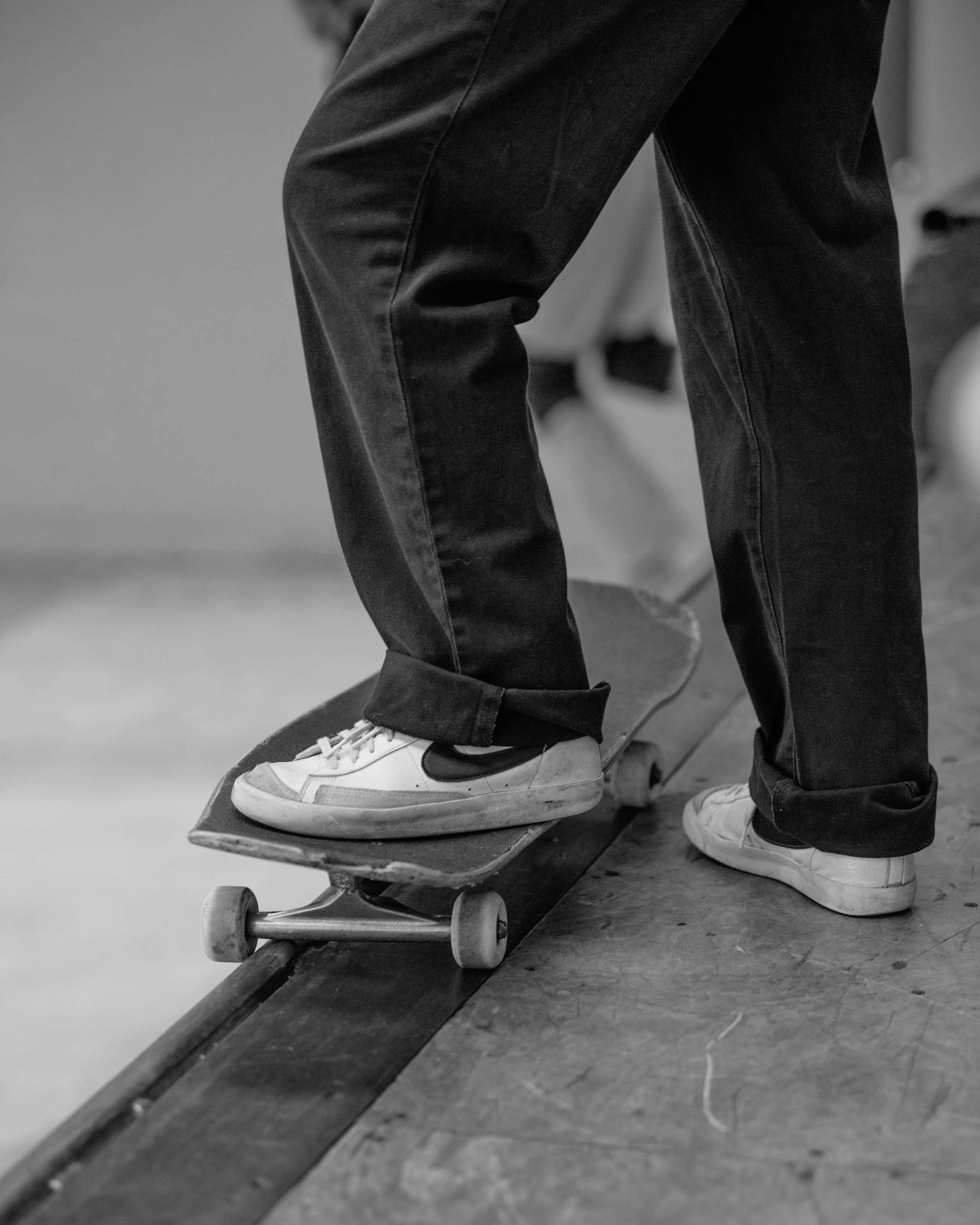 Close-up of a person wearing white sneakers and black pants, balancing on a skateboard at a skatepark.