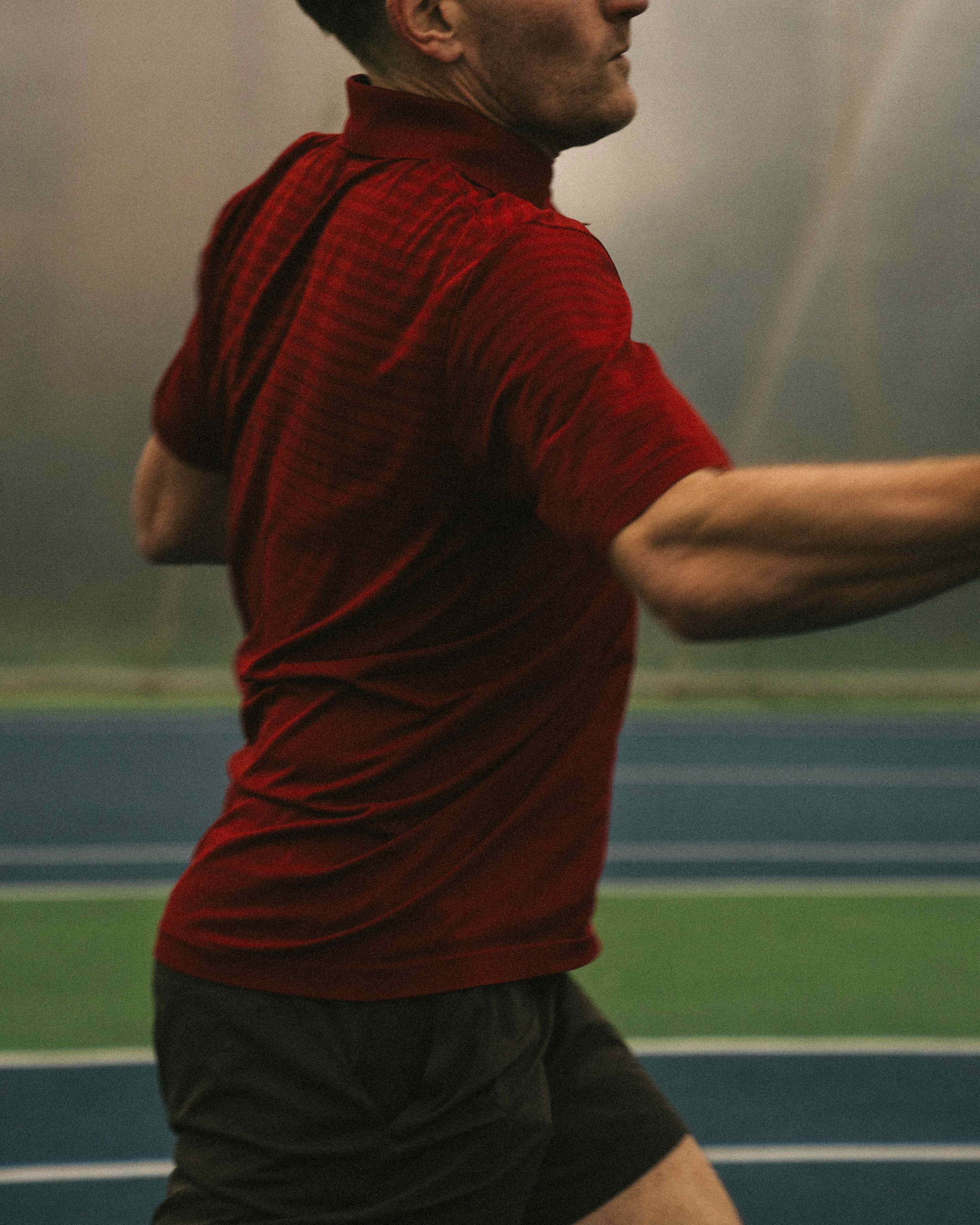 Close-up of a man in a red shirt running on a track.