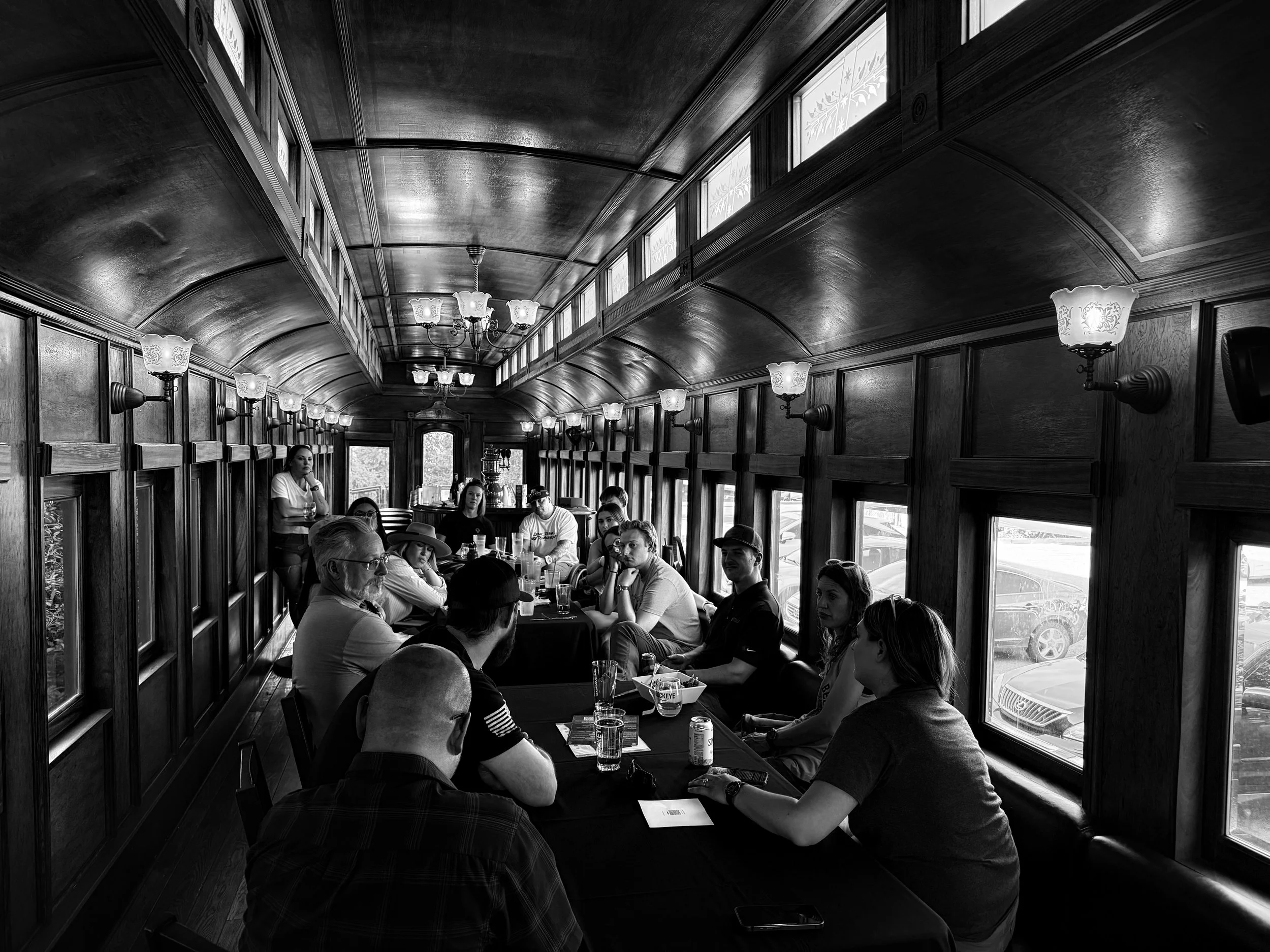 A group of people sitting at tables inside a historic restaurant with wood-paneled walls, decorative lamps, and large windows.