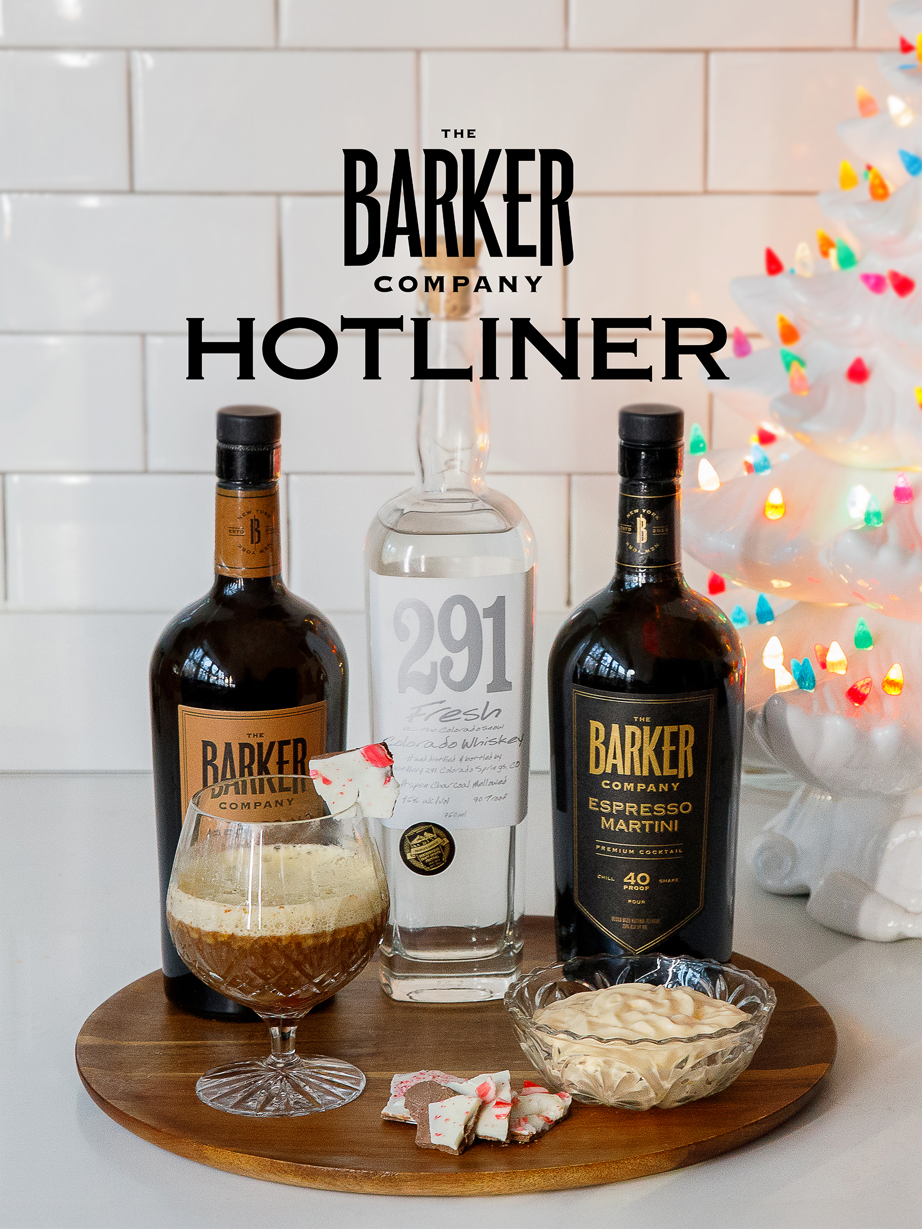 A festive holiday display with bottles of Barker Company alcohol, a cocktail glass with a drink, a bowl of creamy dip, and colorful holiday lights on a white background.