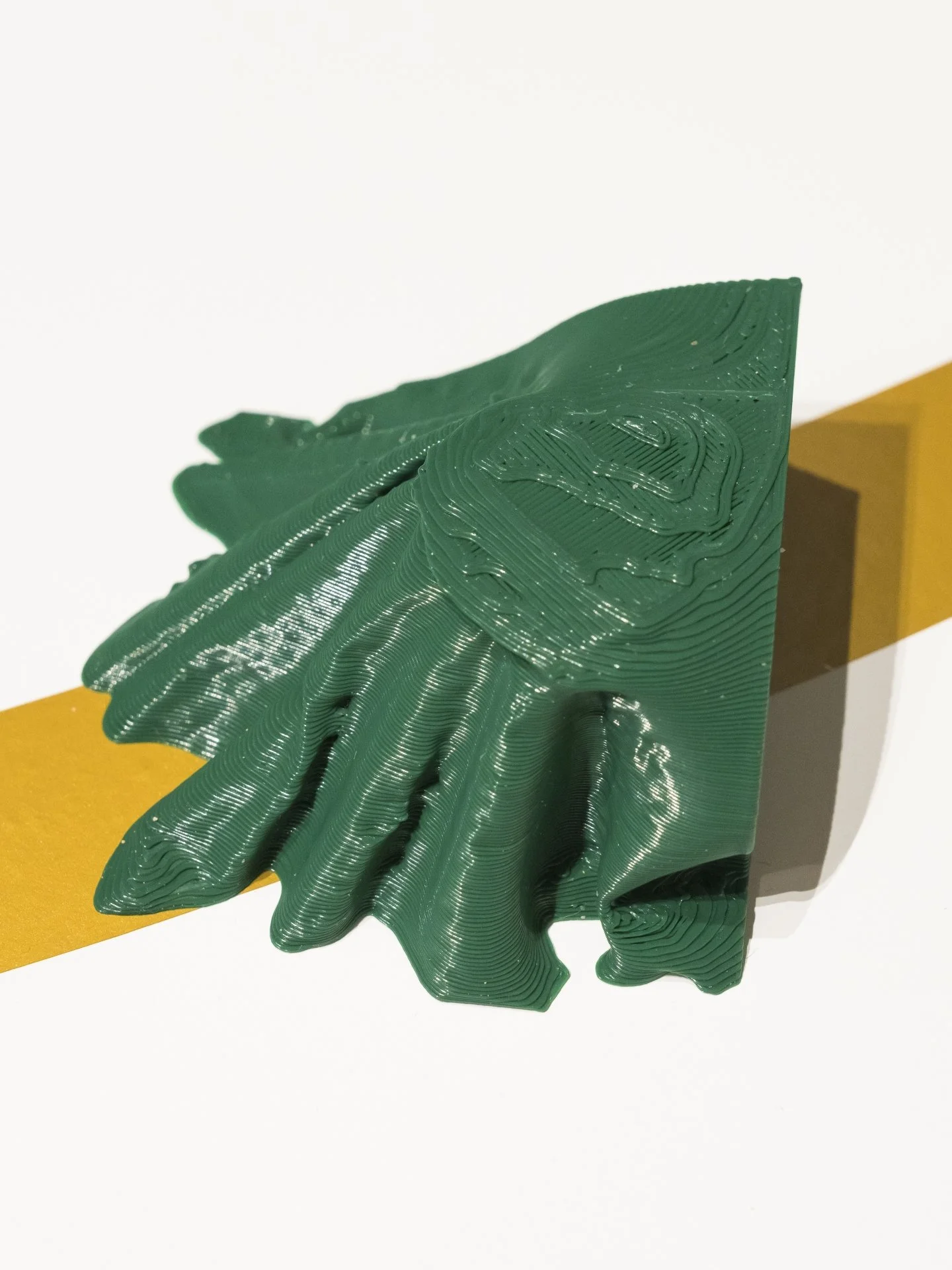 Detail photograph of the 3d prints. a shiny green sculpture resembling a three dimensional topographical map fills the frame. underneath the sculpture is a golden line moving left to right diagonally across the frame.