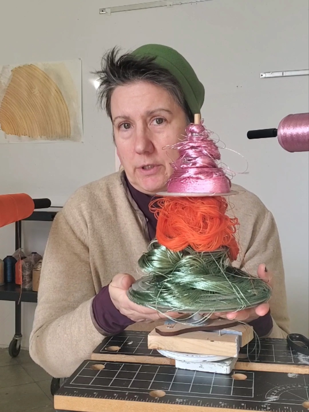 Erika sits in front of her DIY winding mechanism. She is looking at the camera and is holding a sculpture.