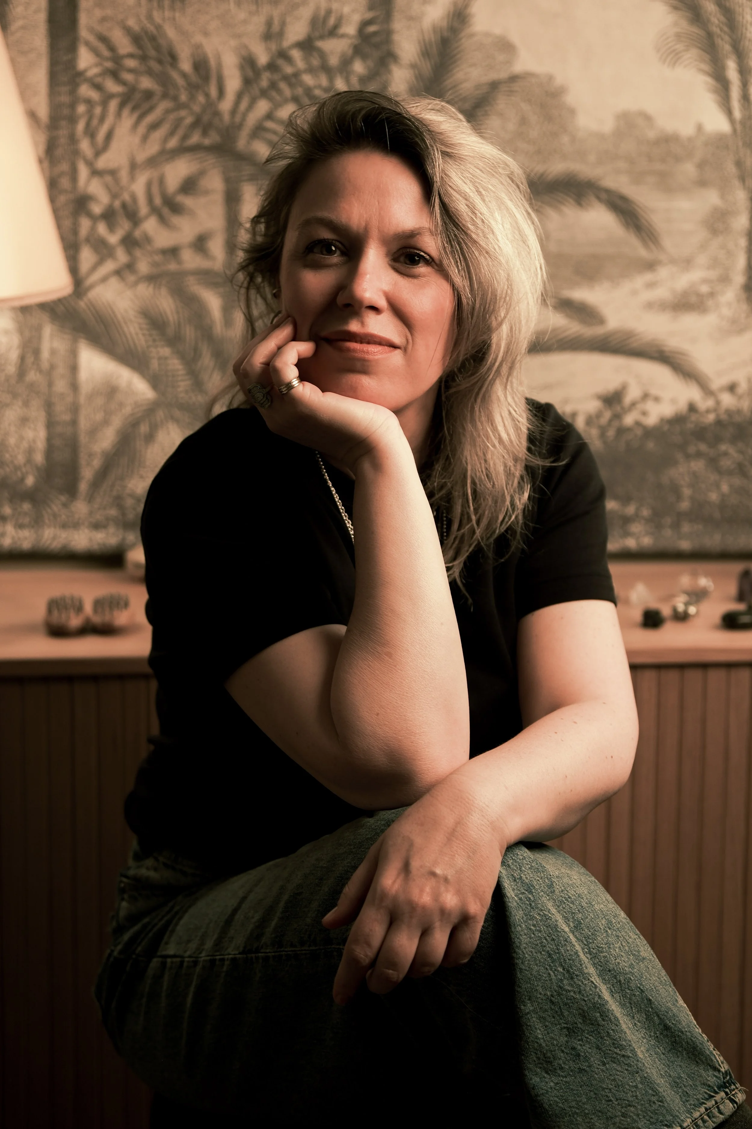 Daphné Bonnet Facialiste LA GARENNE assise et reposant sa tête sur sa main, portant un t-shirt noir, dans dans son studio de massage du visage.