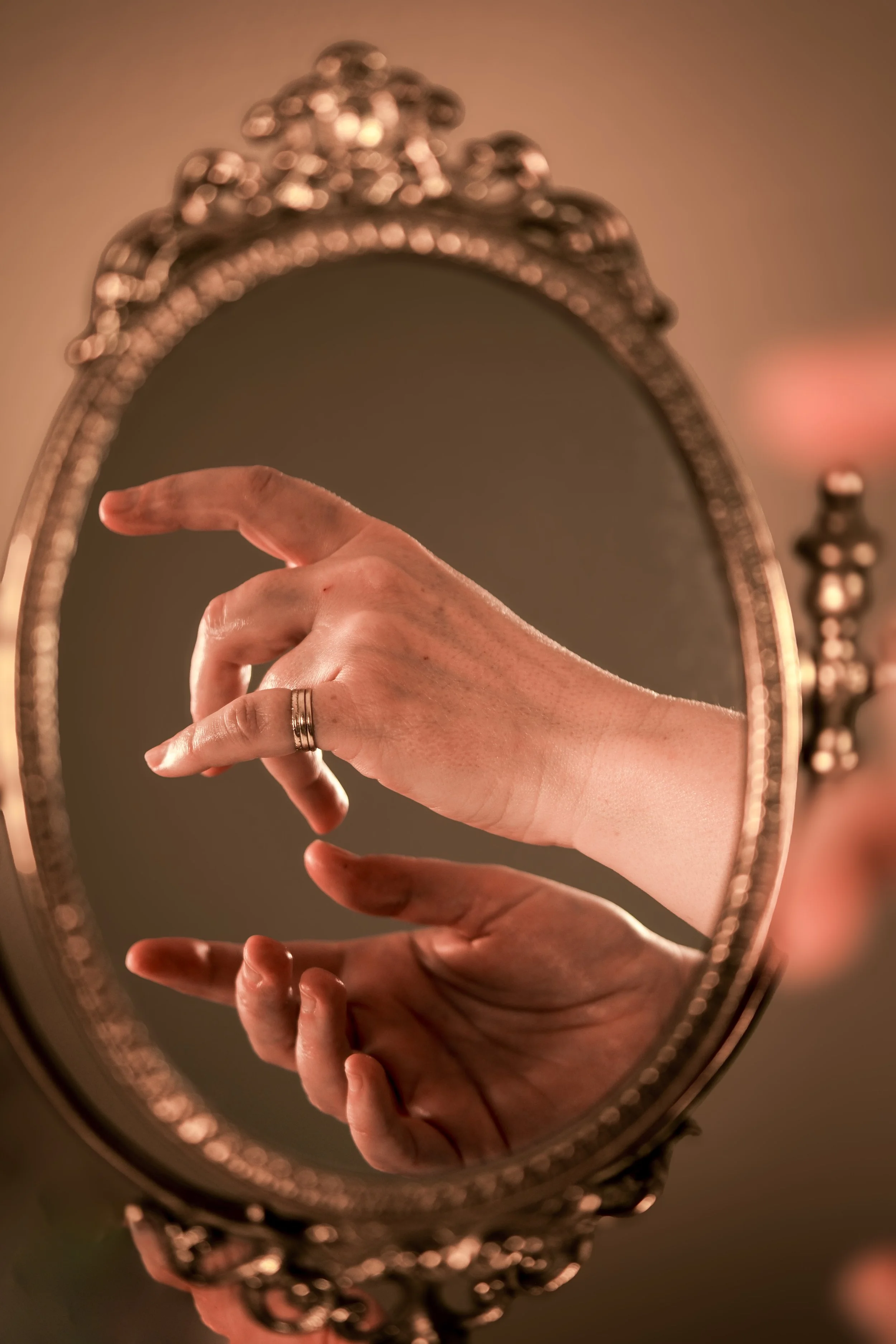 Une main vue dans un miroir ancien, le reflet montre une main avec une bague, en train de faire un geste délicat.