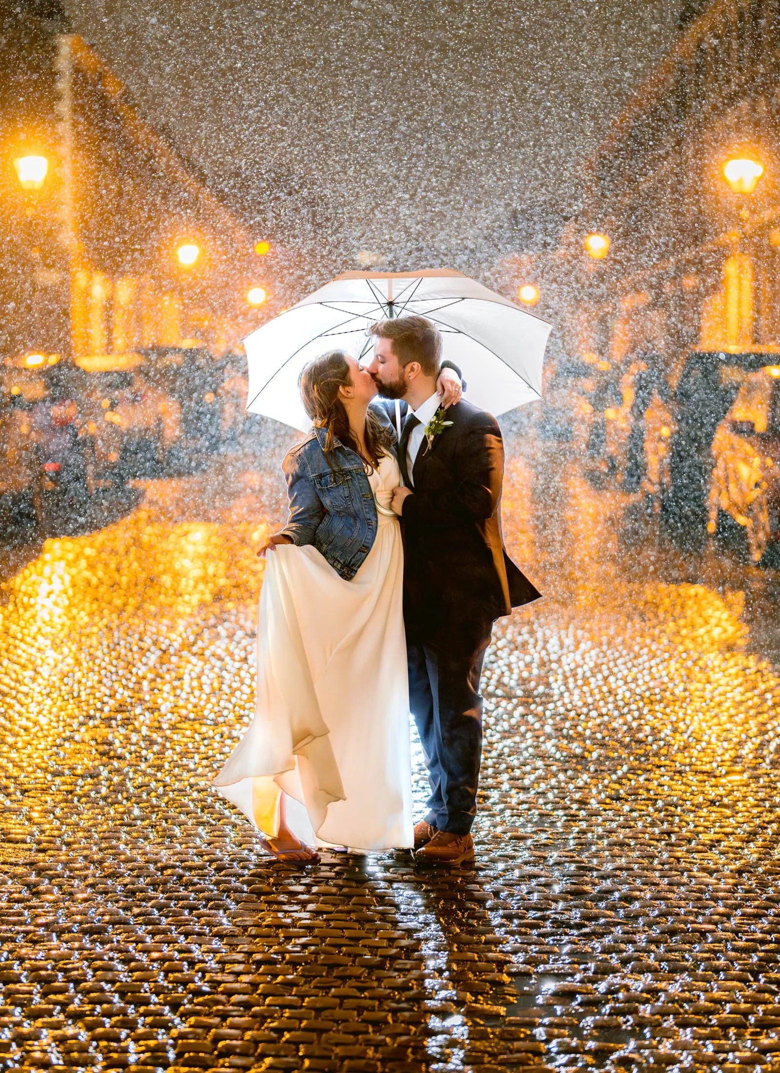 A bride and groom under an umbrella posing for wedding photographs in the rain, Liverpool, UK