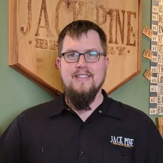 Host Patrick standing against a Jack Pine Brewery sign on the wall.