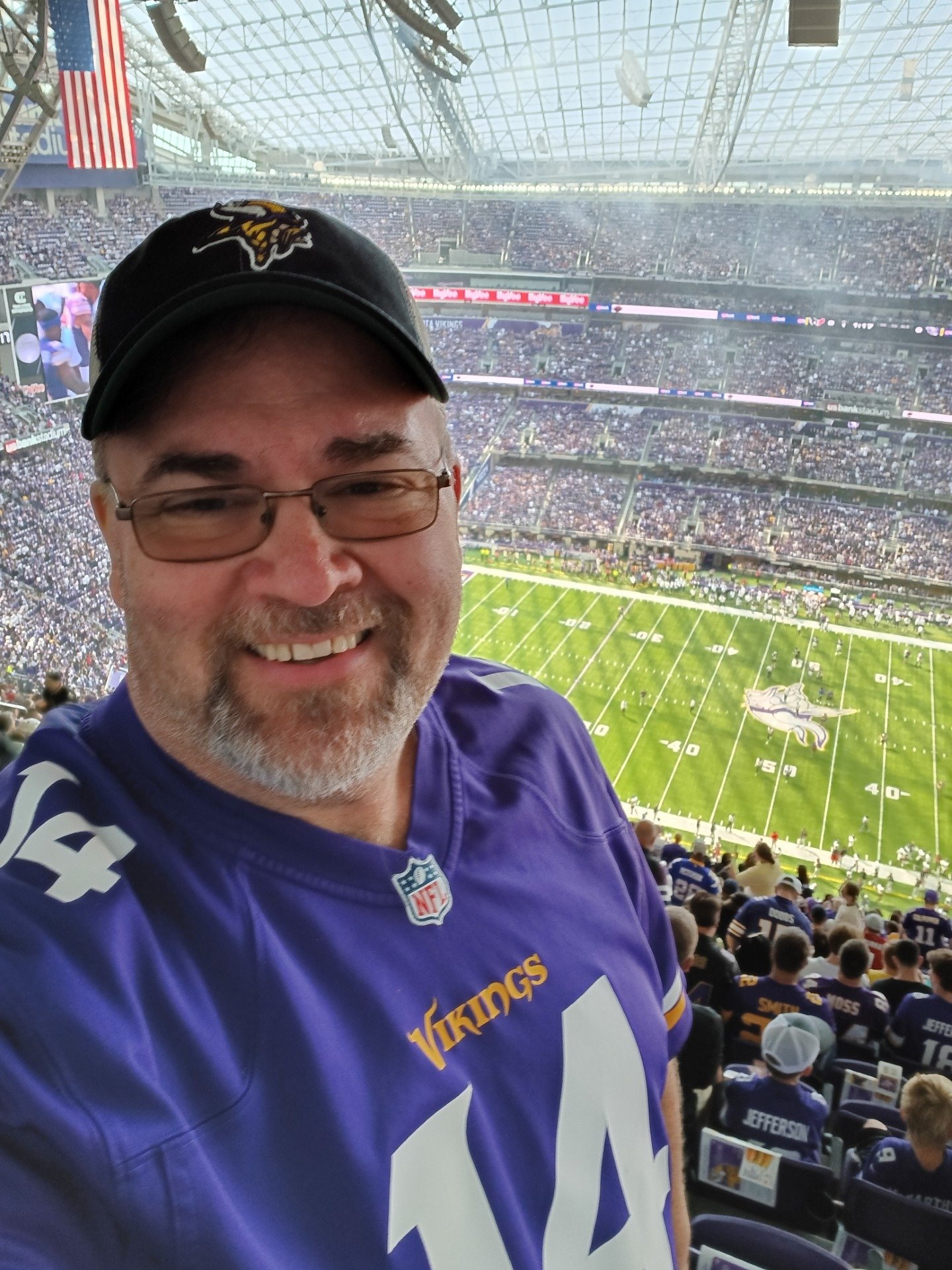 Man wearing Minnesota Vikings hat and jersey at a football game with part of the field in the background