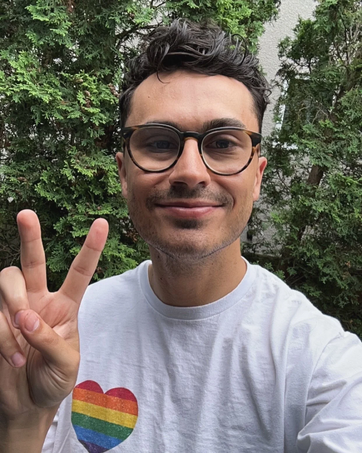 Selfie of young man wearing glasses and hiolding up the peace sign, while sitting outside