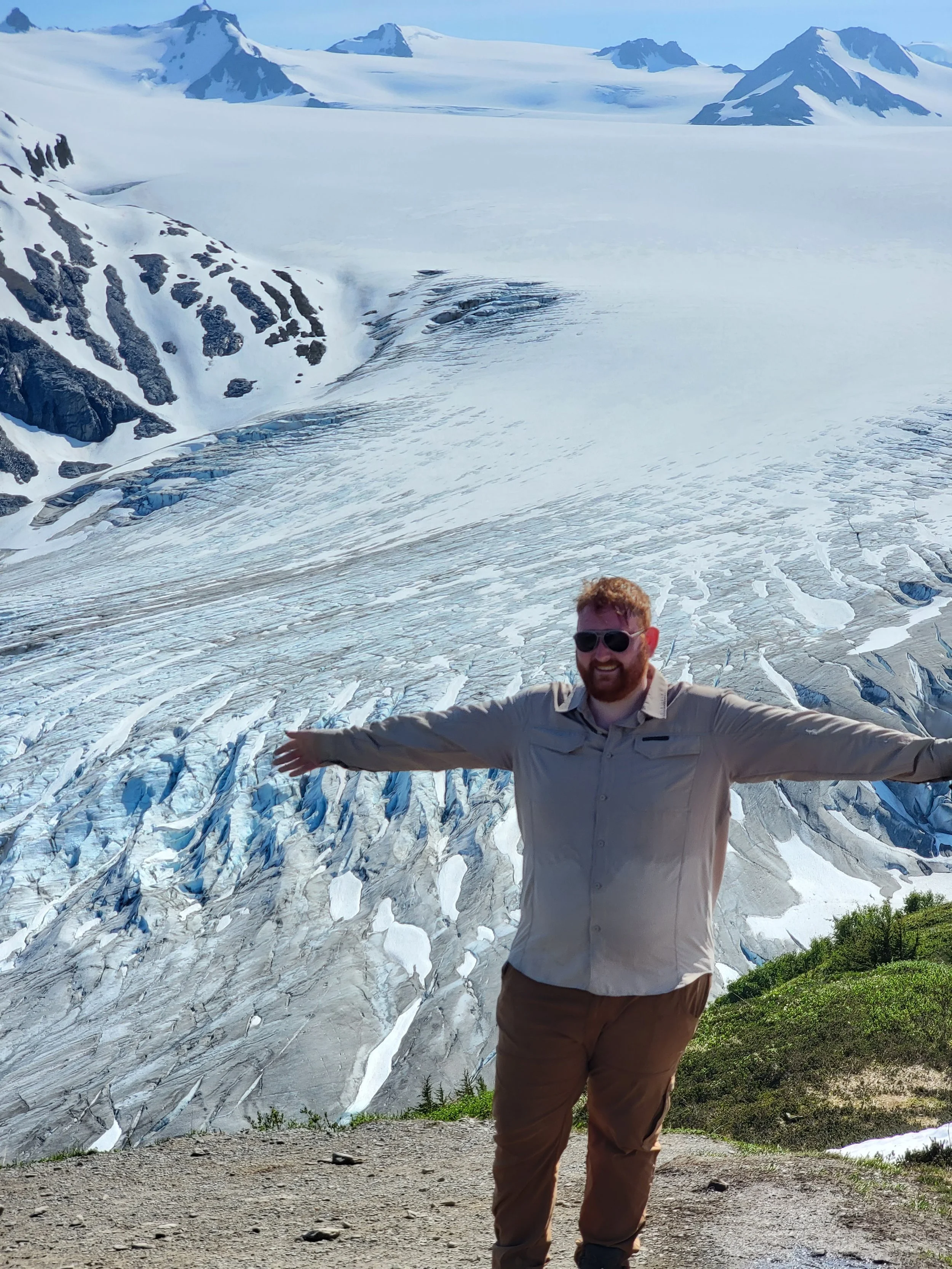 Guy standing in front of a mountain of snow, with his arms stretched out and smiling
