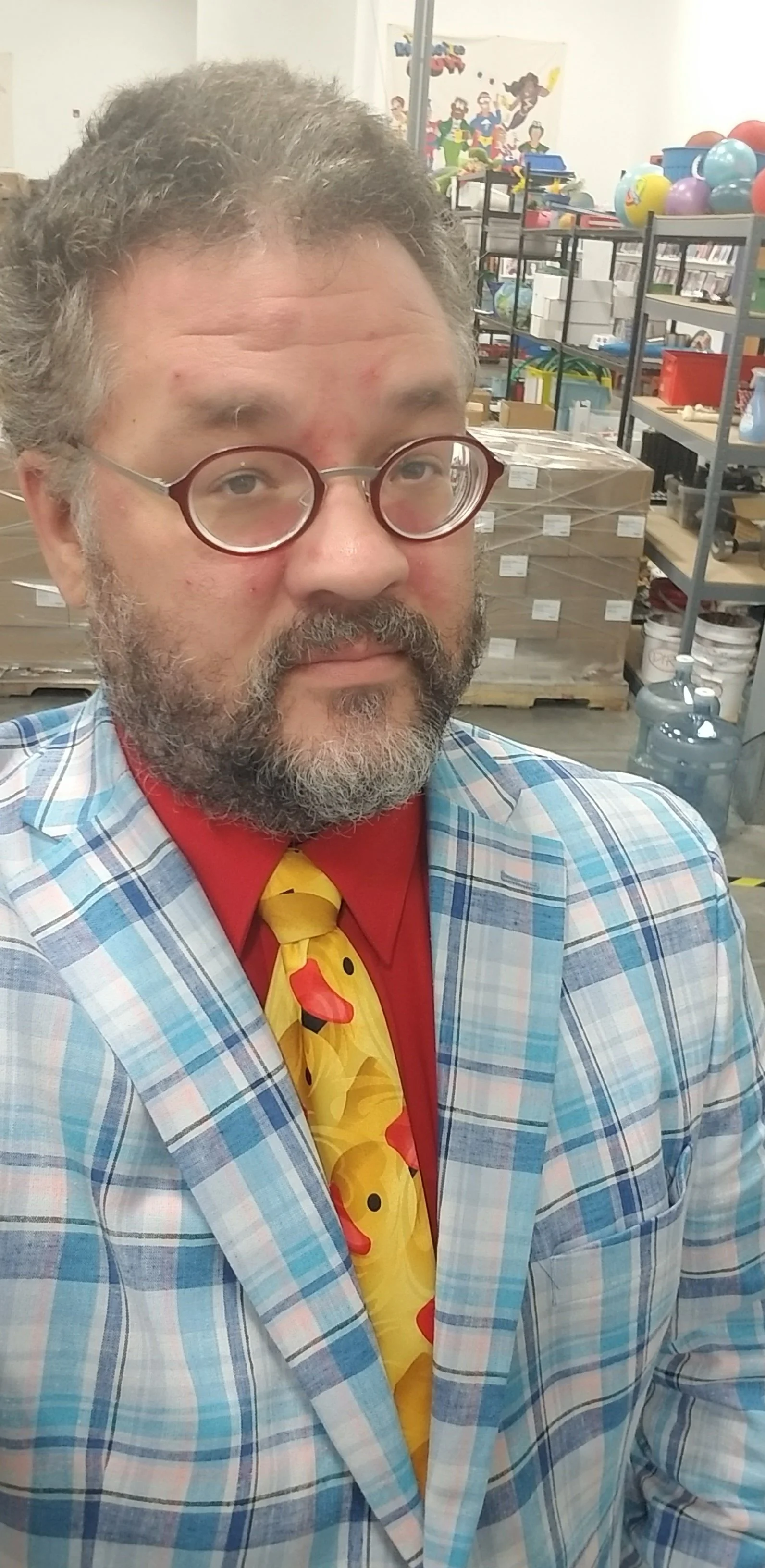 Middle-aged, bearded man wearing glasses with a red T-shirt, plaid blue button up, and rubber ducky tie