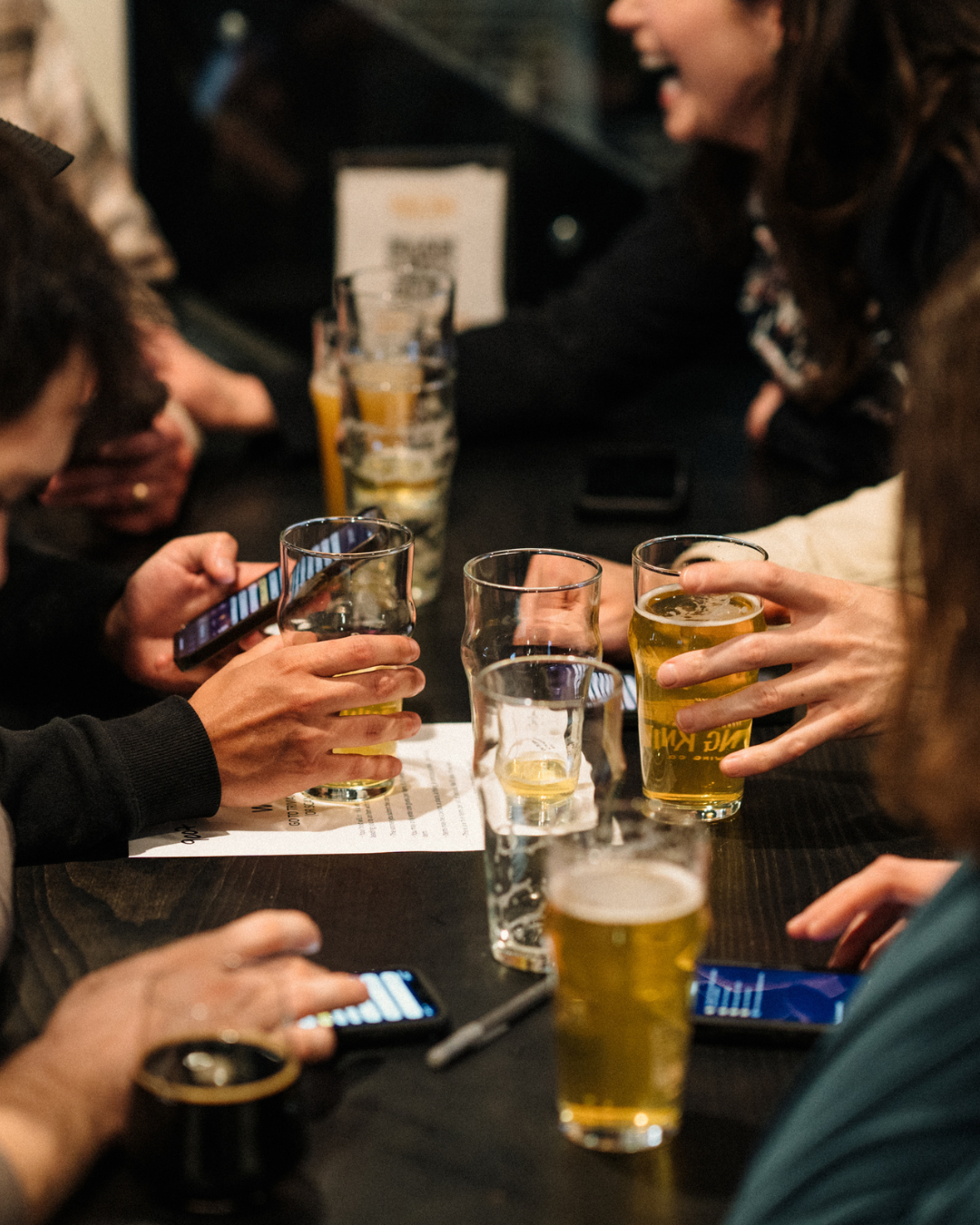 People sitting around a table at a bar or restaurant drinking beer and looking at their smartphones.