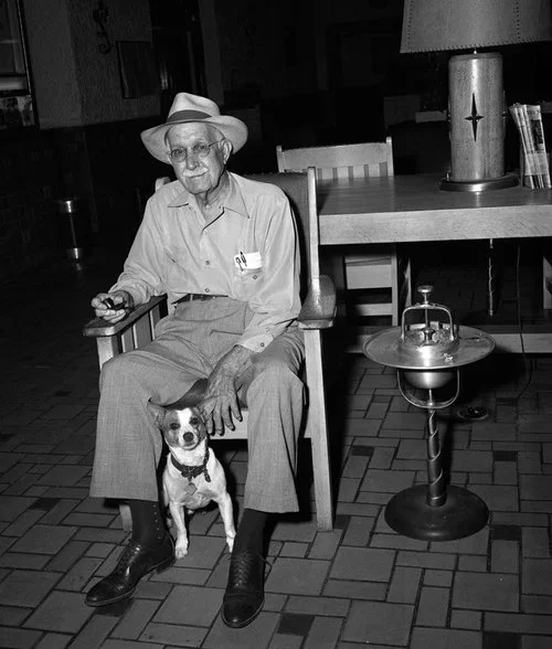 A historical black and white photo of a man sitting with his dog inside the Grand Lobby at Holland Hotel in Alpine, Texas.