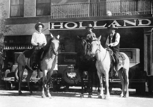 Three horses and their riders pose for a photo outside of the historic Holland Hotel in this black and white photo.