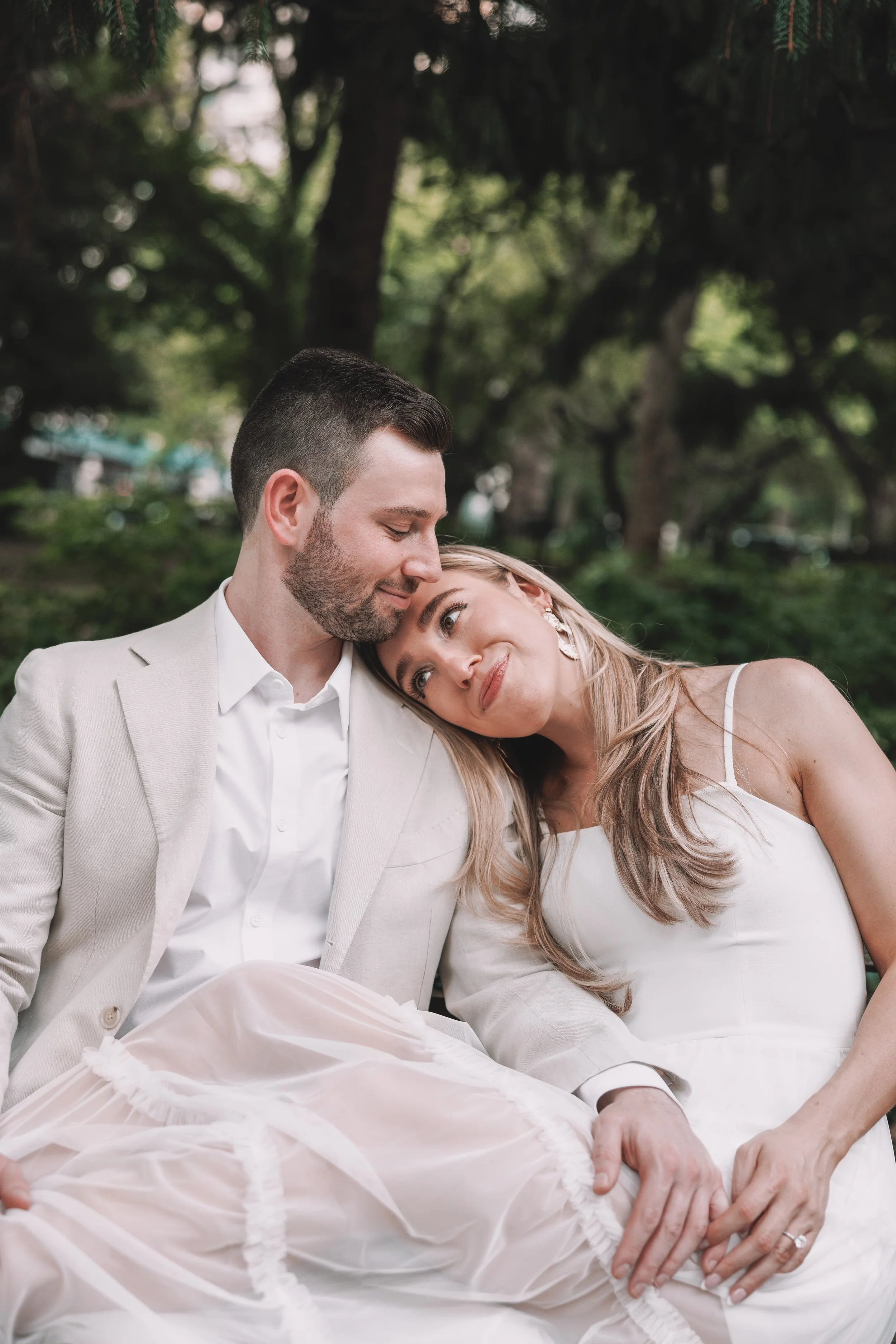 A romantic couple sitting outdoors in a park, with the woman resting her head on the man's shoulder as they share an intimate moment.