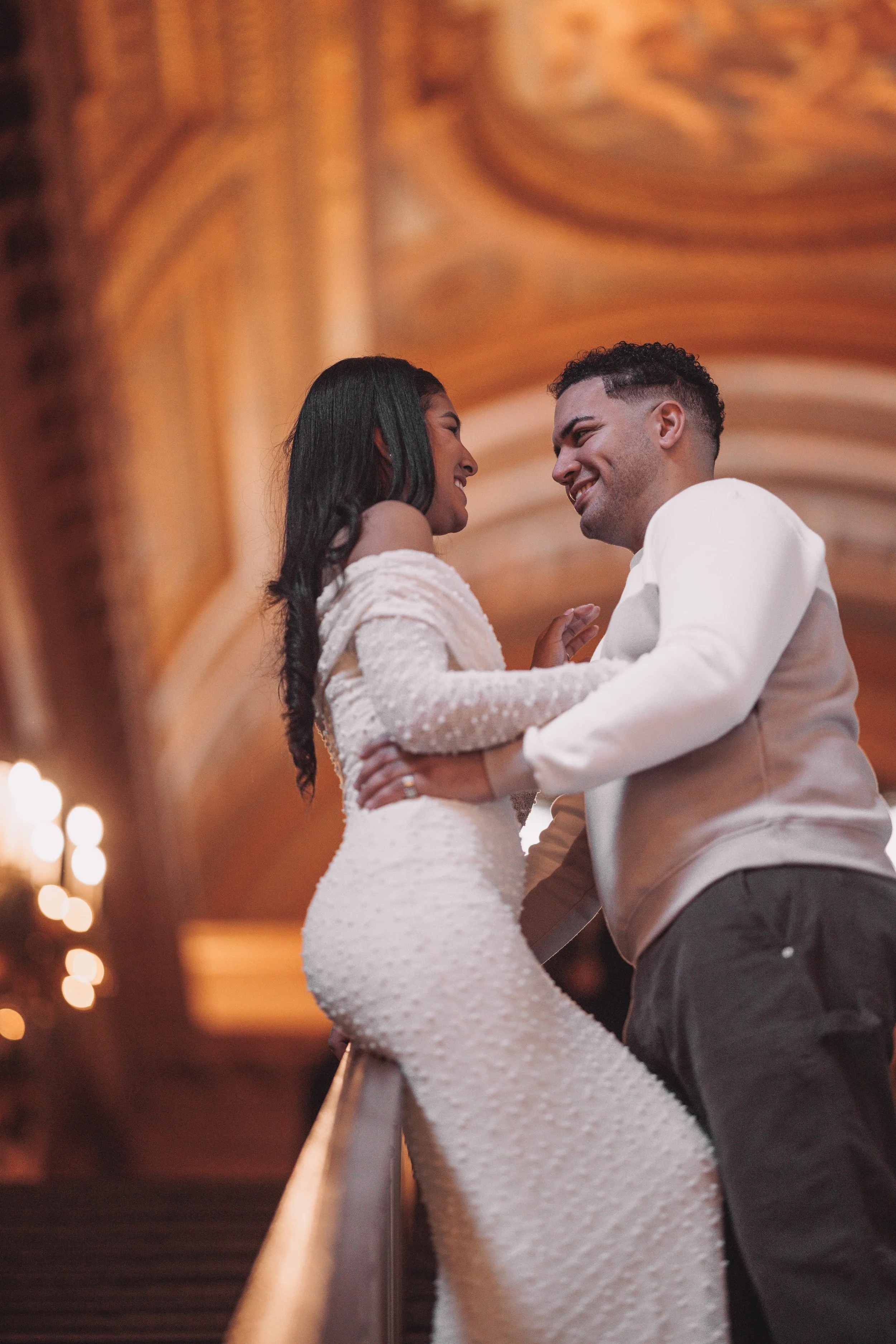 A couple is dancing closely together indoors, with warm lighting and ornate ceiling details visible in the background.
