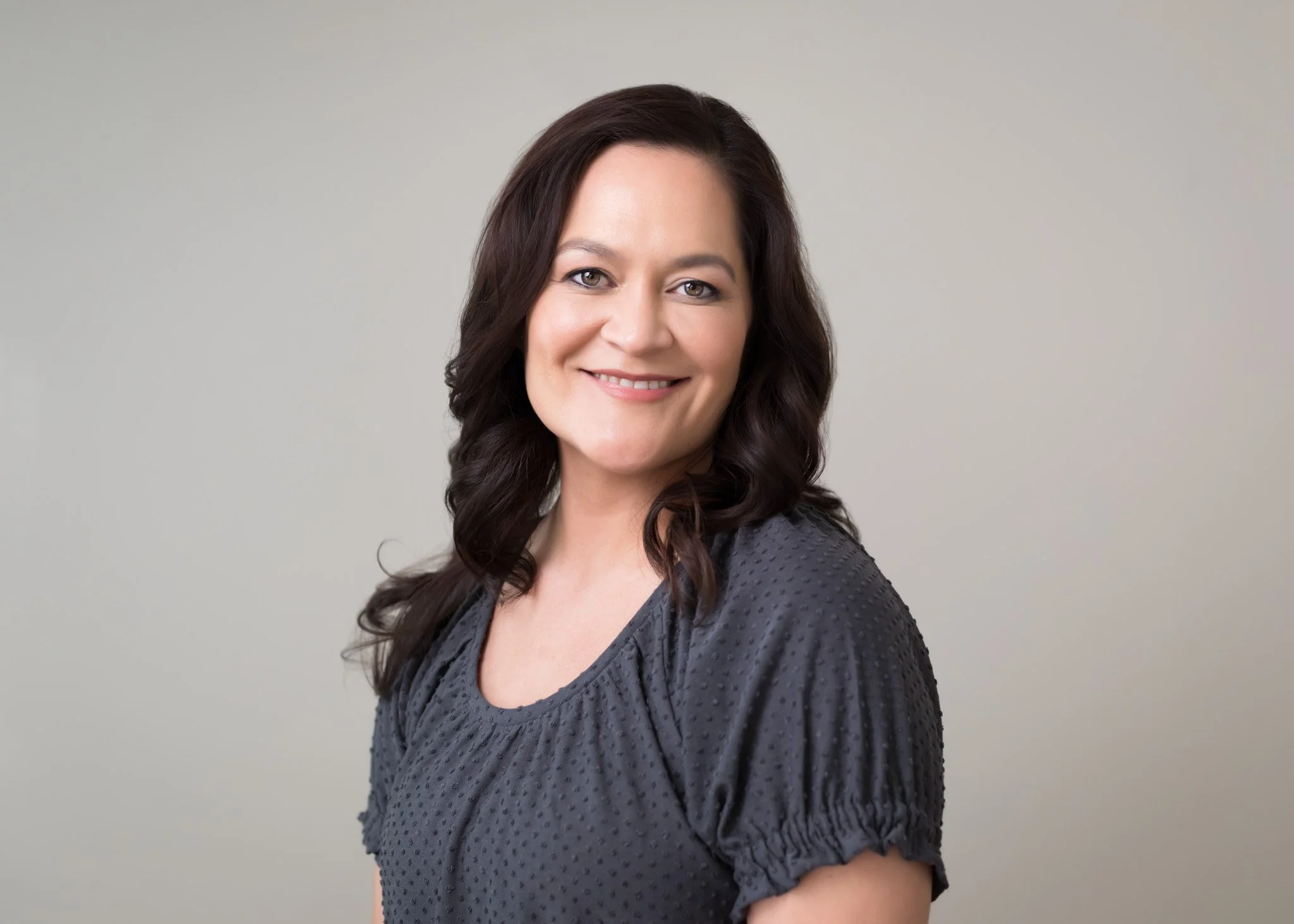 Professional studio headshot of Yvonne Swann smiling, wearing a dark grey textured blouse against a neutral grey background.