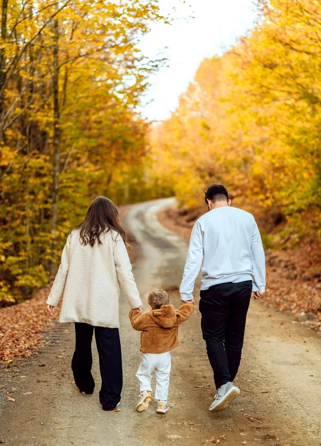 Family walking together along a scenic dirt road surrounded by colorful fall foliage.