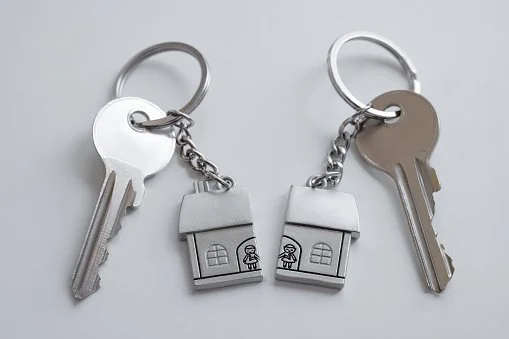 A couple of keys attached to separate keychains with split house half-shapes, suggesting broken marriage, property division, separation and divorce.