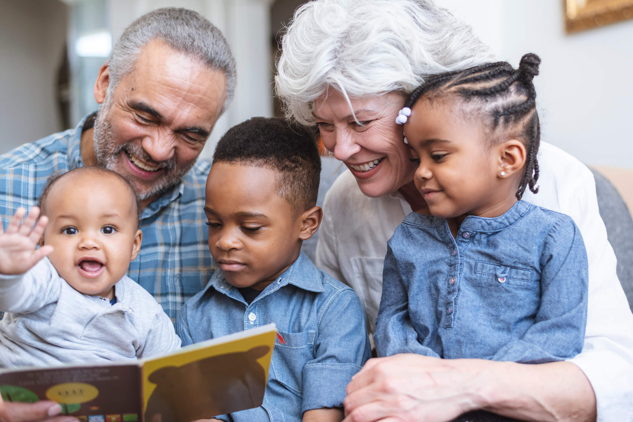 Grandparents reading a children's book with three young grandchildren, smiling and engaging with the book. A stock photo on theme of multi-generational family in the context of a family law firm website.