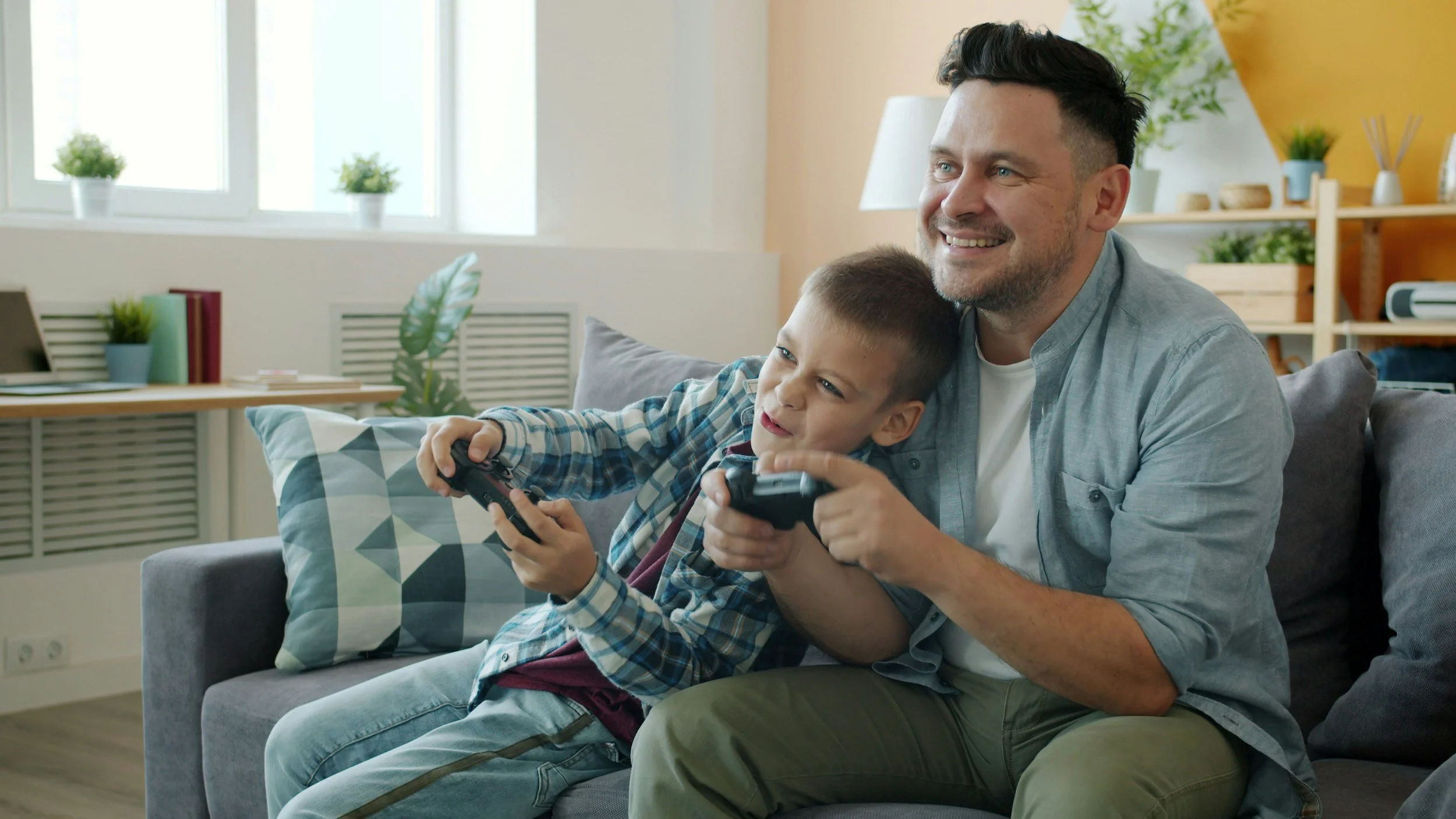 Father and son on a couch in a living room enjoying time together playing a multiplayer game.