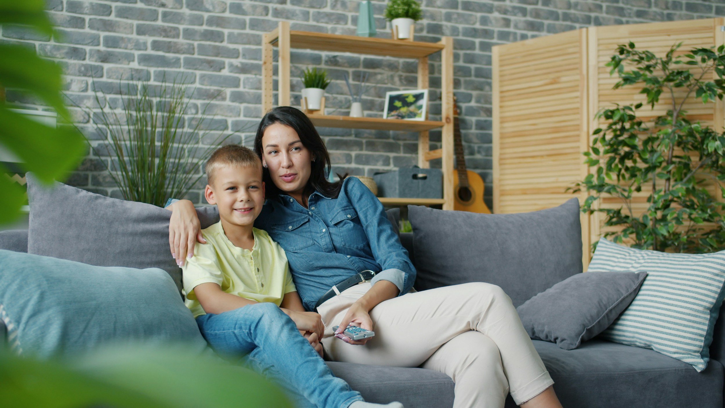 Mother and son sitting together on a living room couch, smiling, talking, enjoying some quality time.