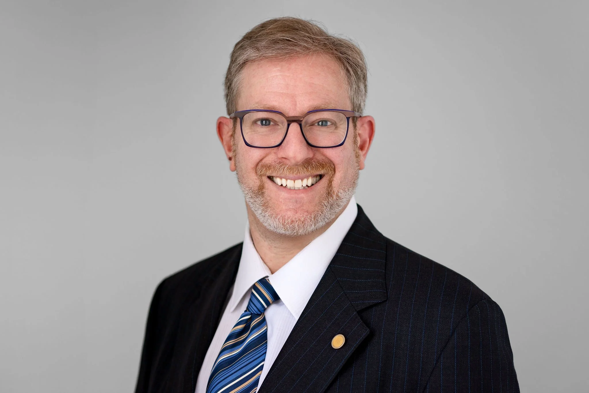 Professional headshot of Avram Joseph, Senior Counsel, Family Lawyer,  in suit, tie and glasses, on a grey background.