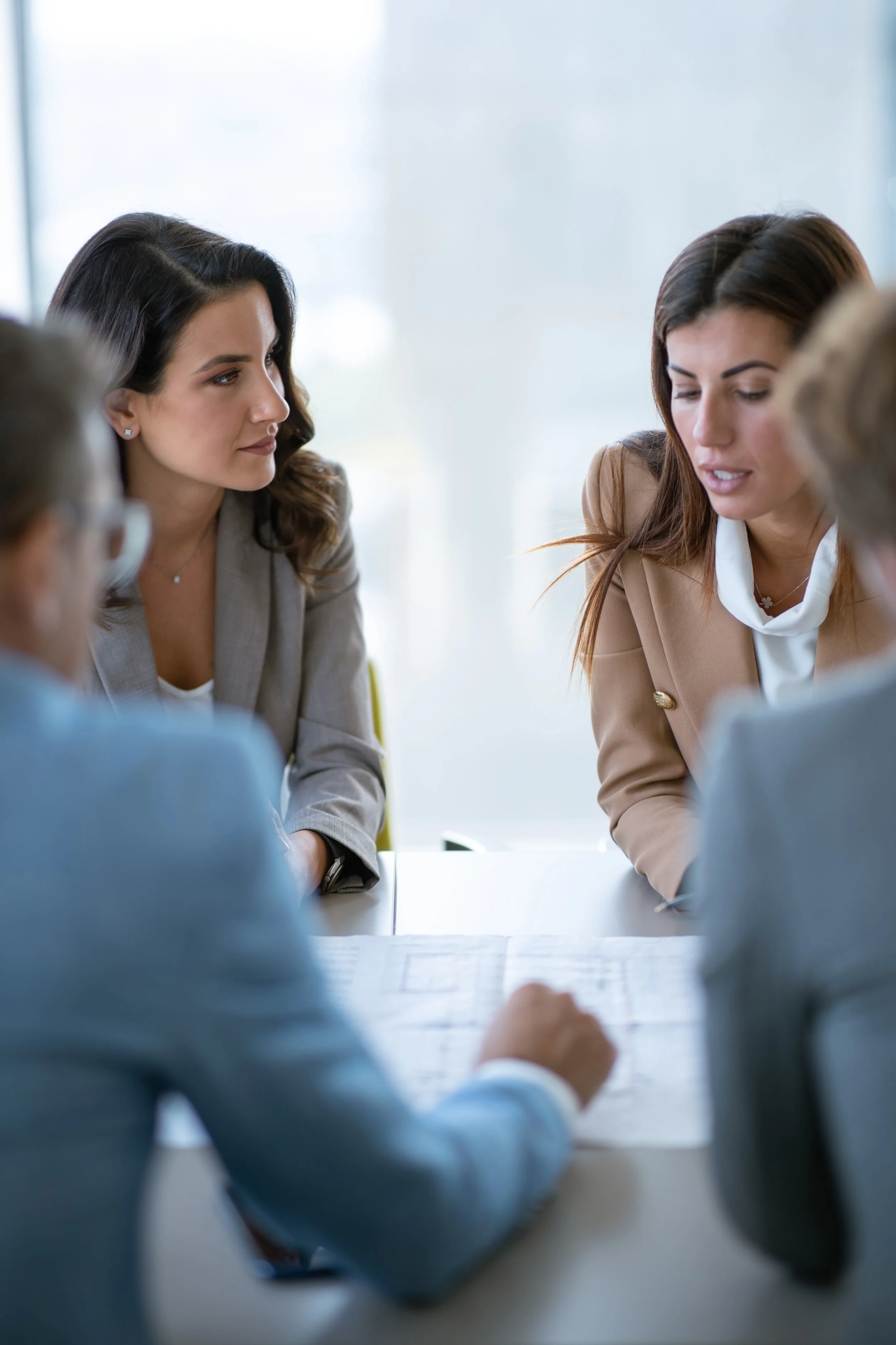 A group of professional looking people, three women and a men, perhaps a couple meeting lawyers or mediators, discussing things over legal documents in a bright modern space.