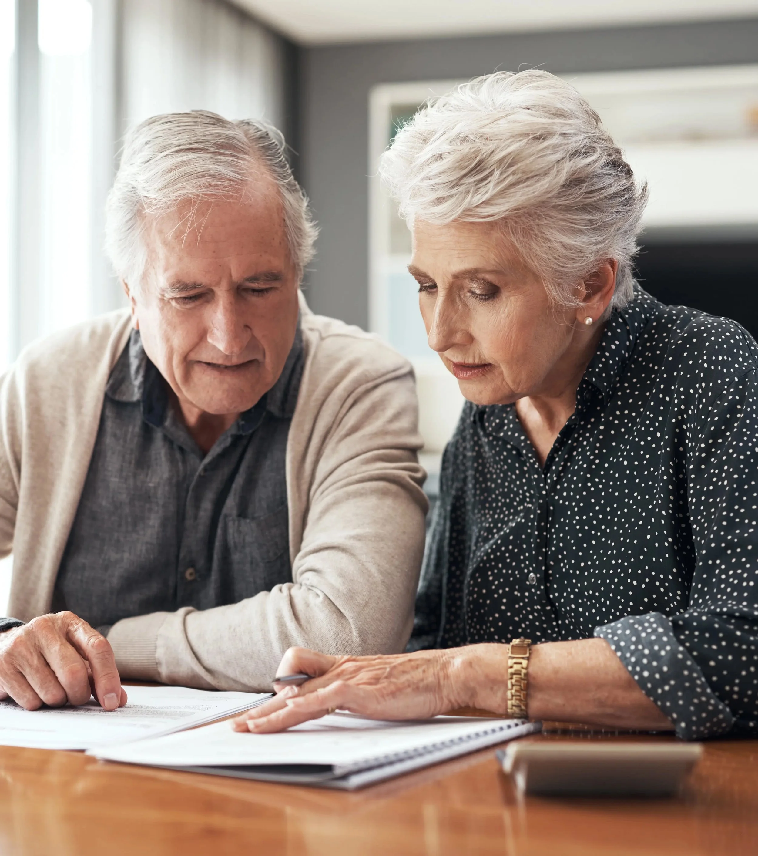 An elderly man and woman reviewing legal documents, perhaps a will, together at a table, indoors, with natural light coming in. A stock photo.