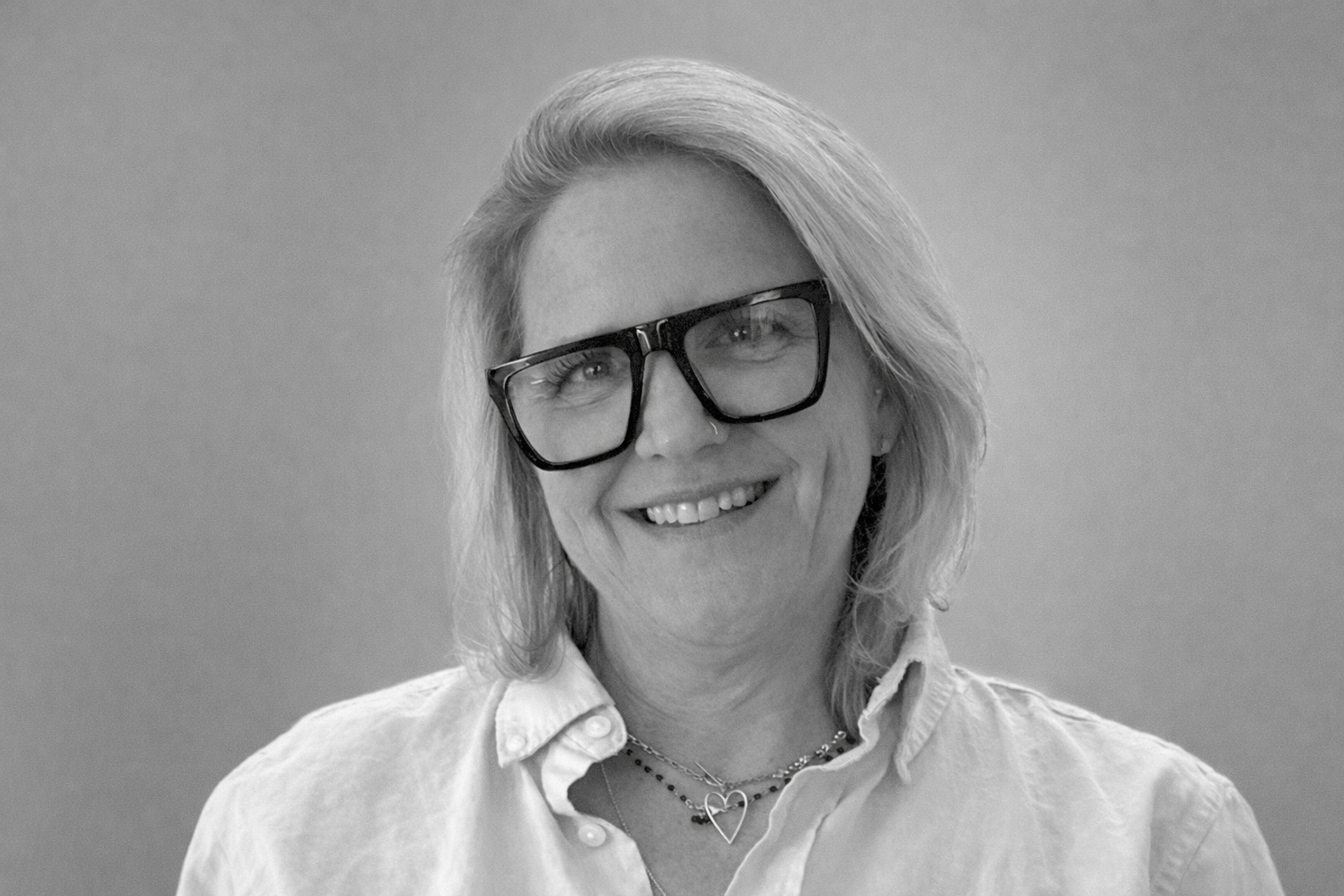 Professional headshot photo of Kira Berry smiling. Black and white with grey background.
