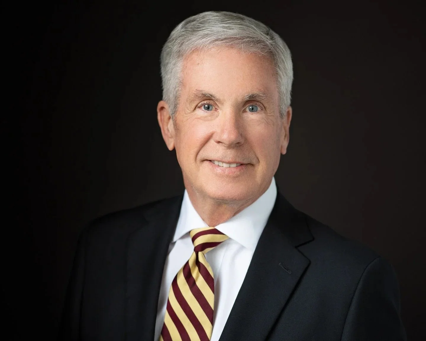 Headshot of John C. Drake, President and Founder of Drake Law, wearing a dark suit and a striped tie, smiling confidently.