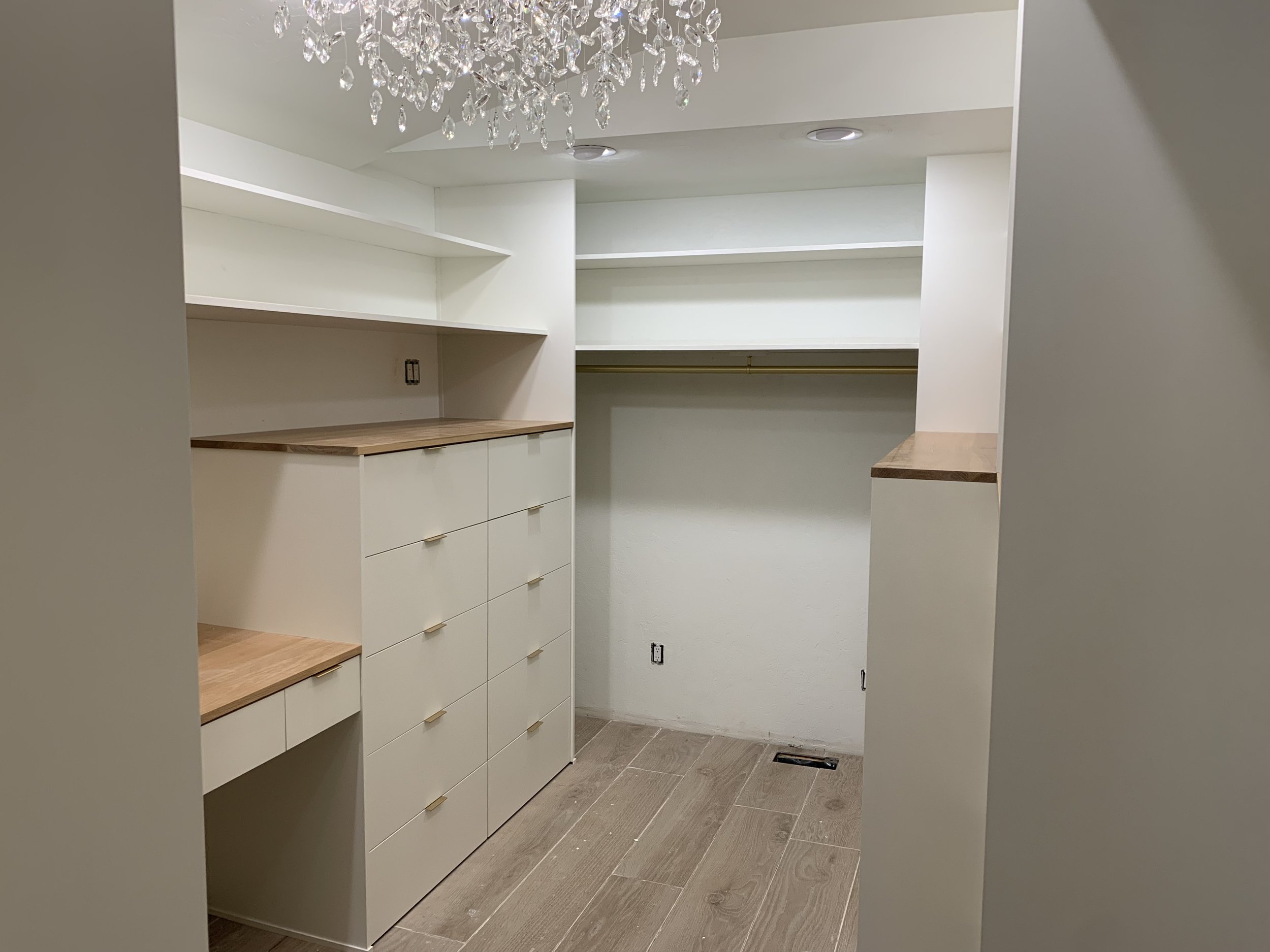 Empty walk-in closet with white cabinets, wooden countertops, open shelving, hanging rod, and a chandelier overhead.