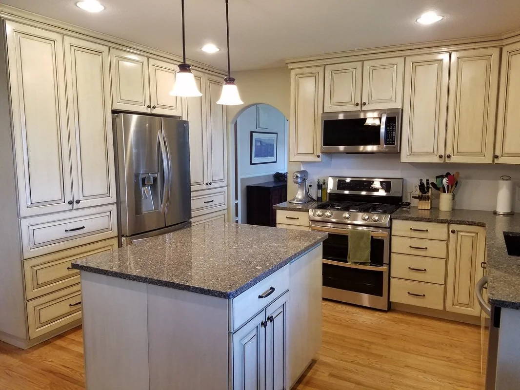Kitchen with cream-colored cabinets, stainless steel refrigerator, microwave, and oven, granite countertops, pendant lights over island, and hardwood floors.