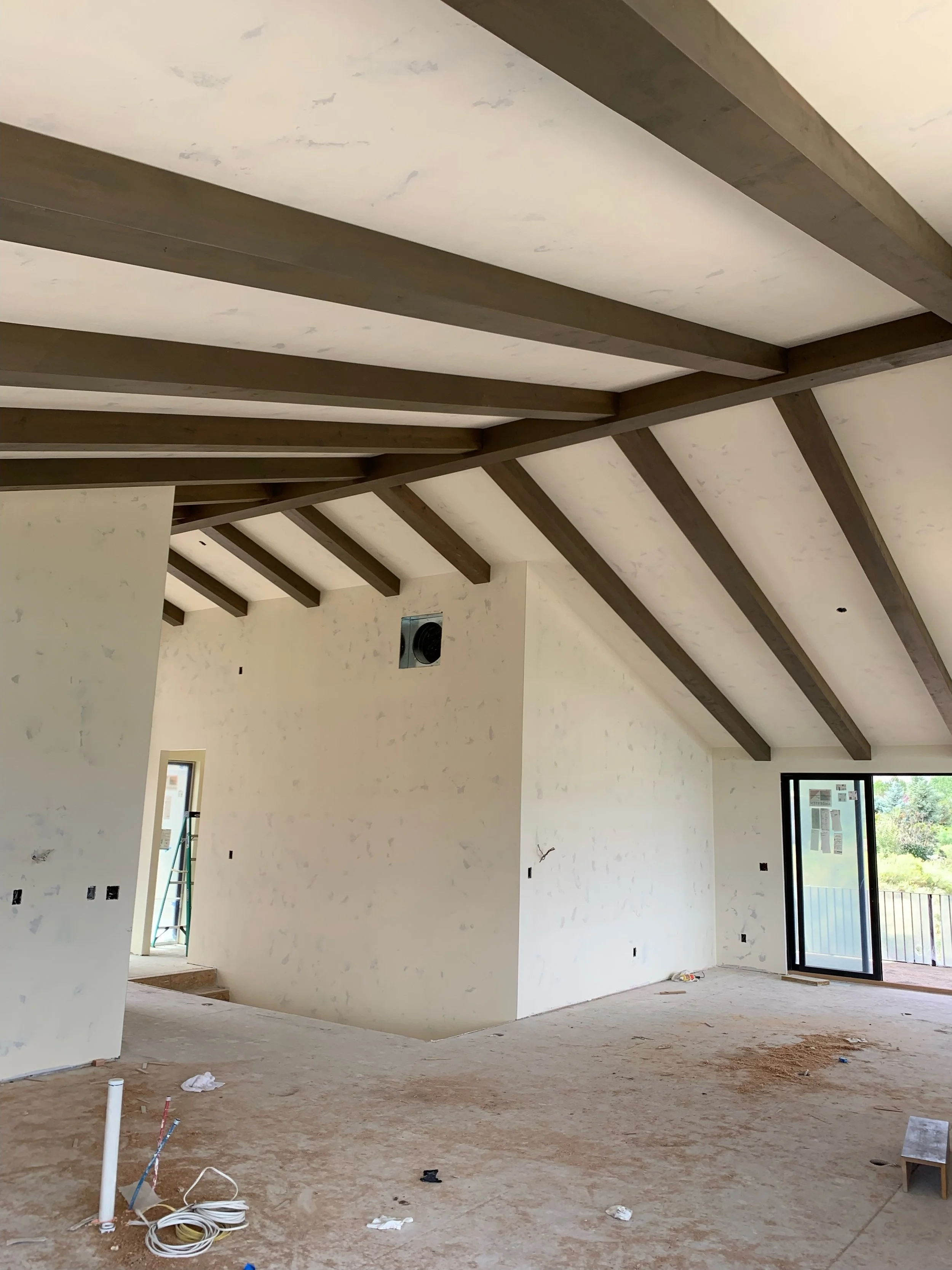 Interior of a house under construction with exposed wooden beams on the ceiling, unfinished walls, and construction debris on the floor.