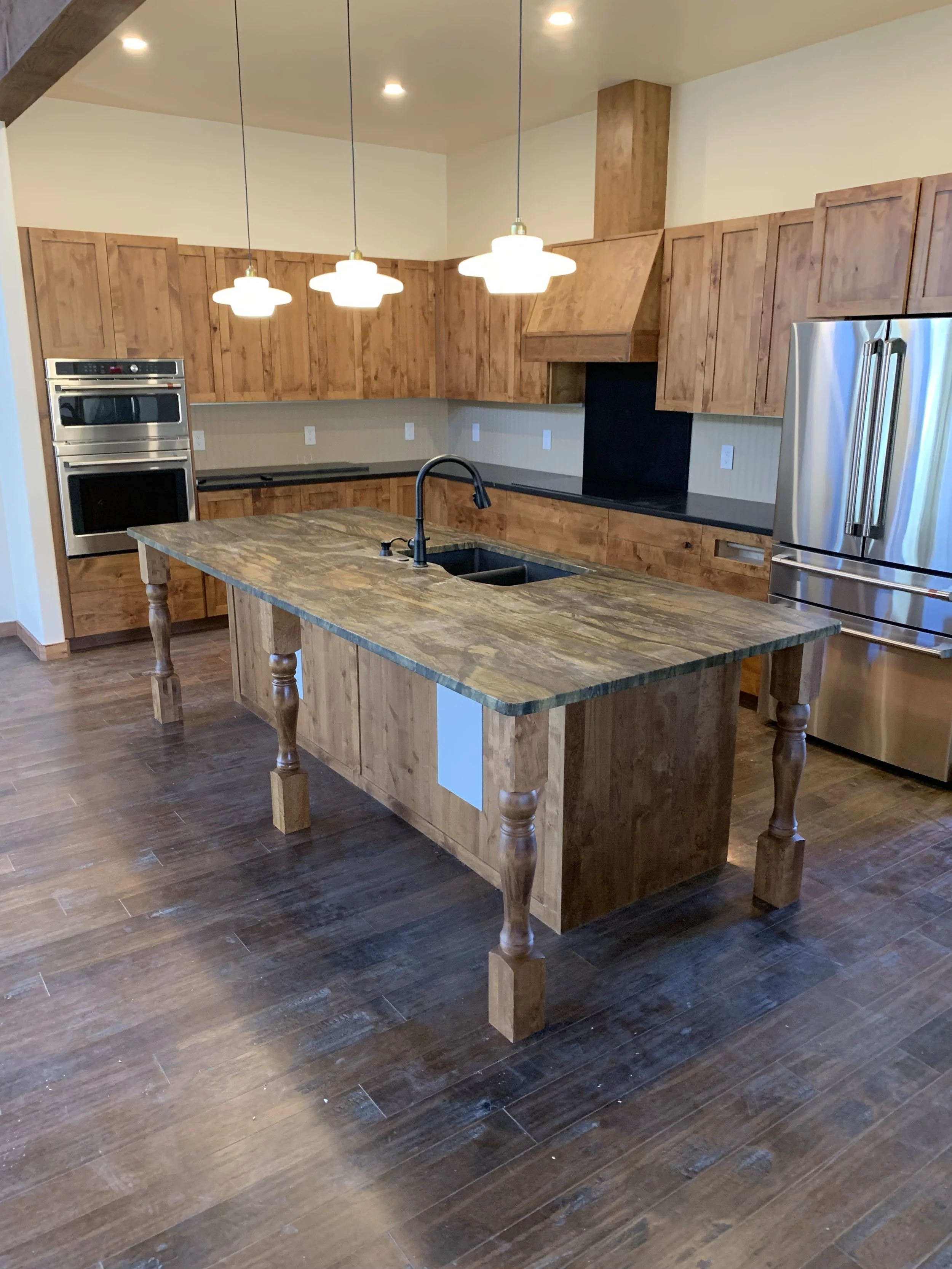 Modern kitchen with wooden cabinets, a central wooden island with a granite countertop, stainless steel appliances, pendant lighting, and dark wooden flooring.