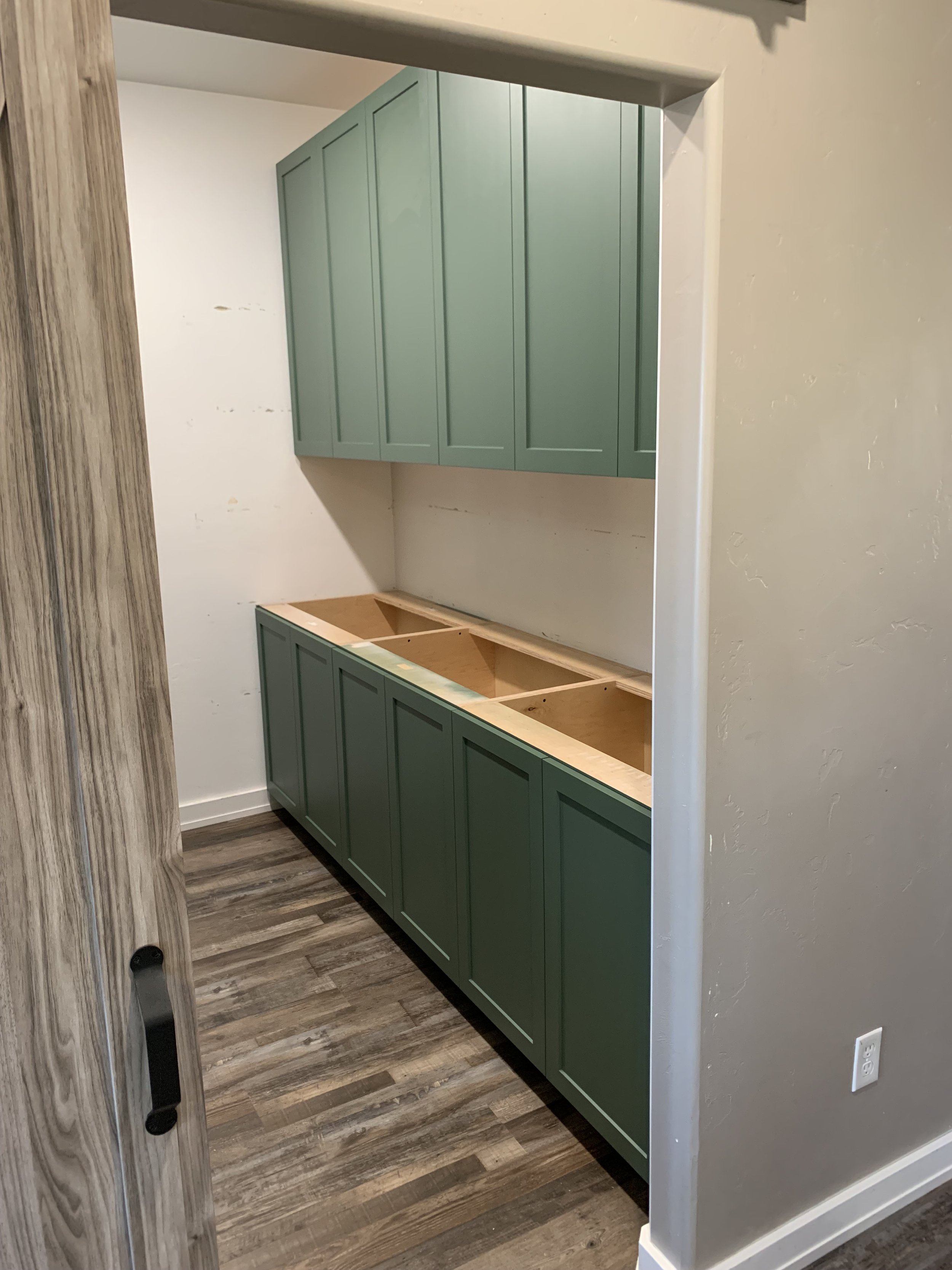 Interior view of a partially completed or renovated kitchen area with green upper and lower cabinets, and an empty space for a countertop.