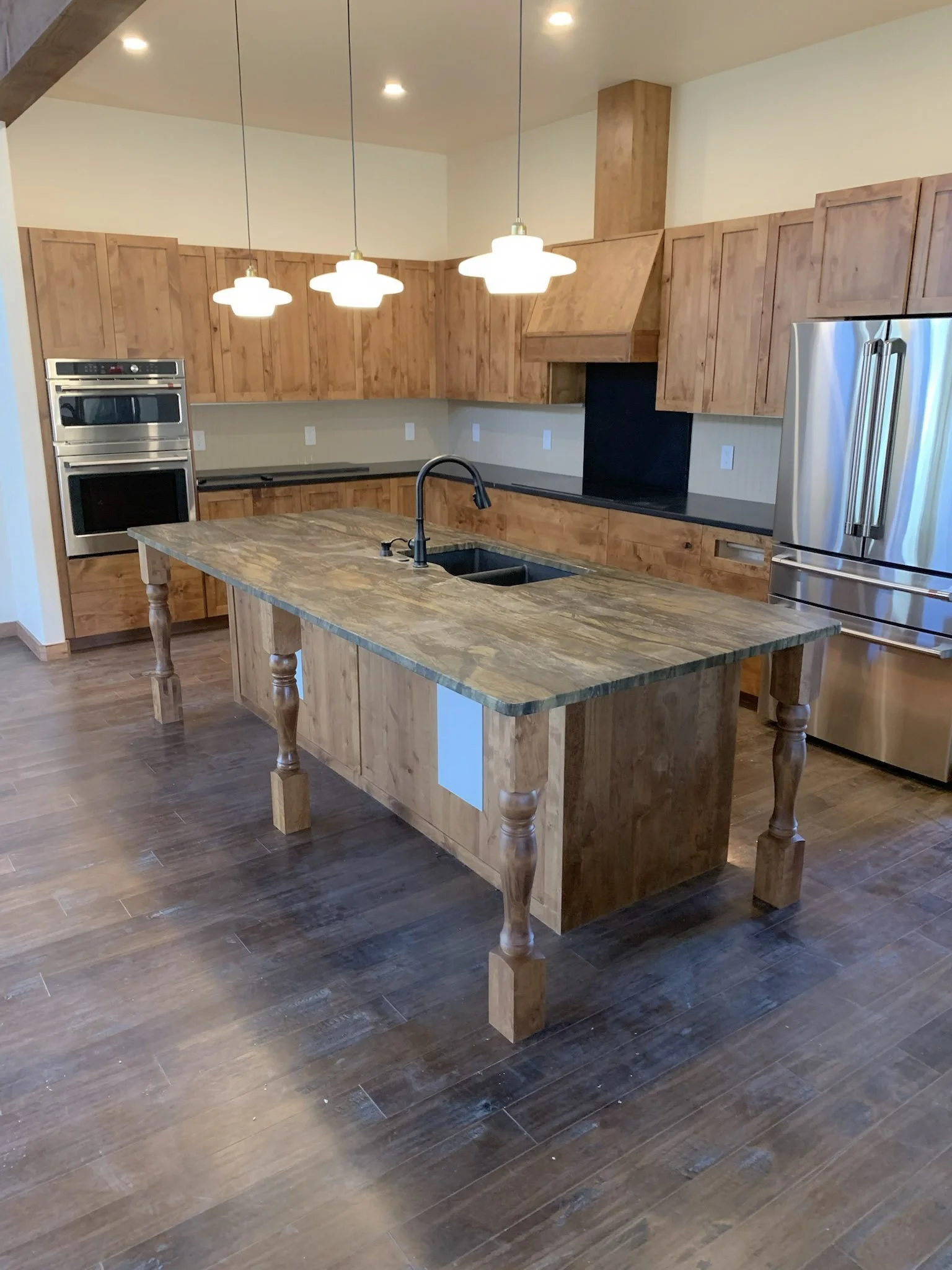 Kitchen with wooden cabinets, a wooden kitchen island, stainless steel refrigerator, built-in double oven, and pendant lights