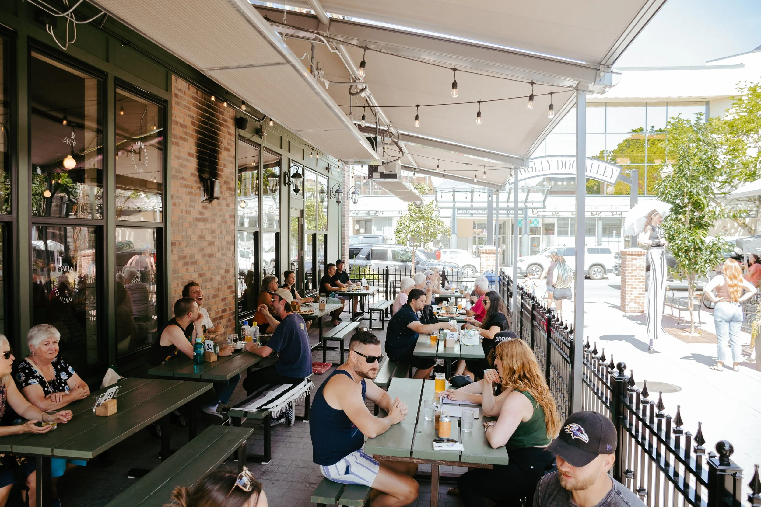 People dining at an outdoor restaurant patio under a white canopy on a sunny day.