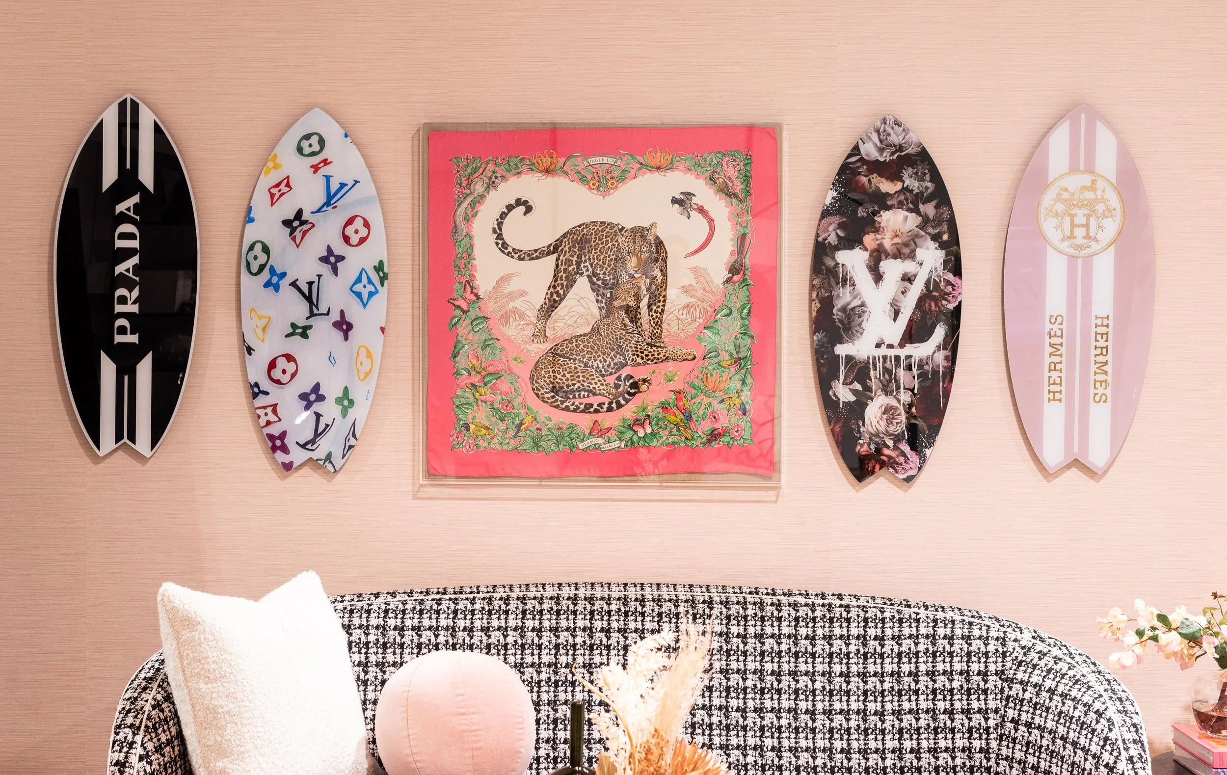 Decorative wall with five surfboard-shaped art pieces, a central framed art piece of two leopards, a floral patterned