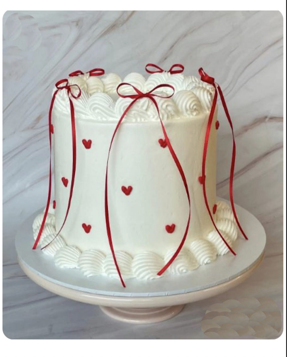 Gluten Free tall white cake decorated with red ribbons and small red heart-shaped accents, placed on a cake stand against a marble background.