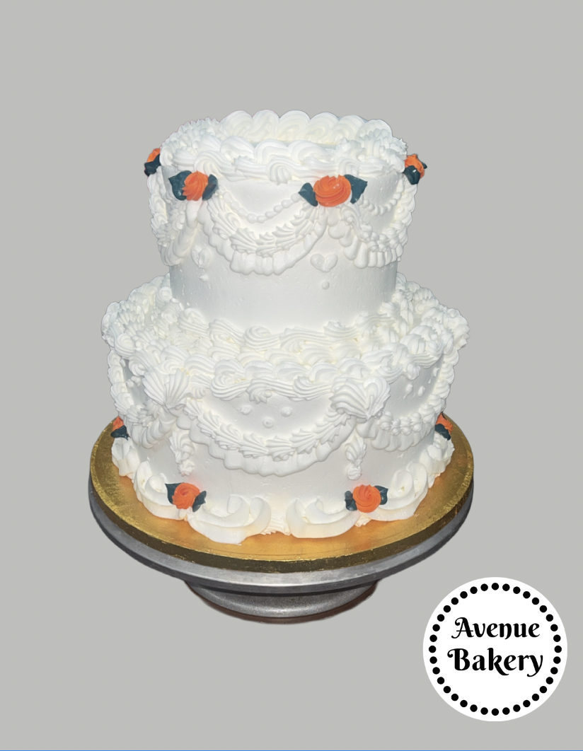 Gluten Free Custom Cakes in SLC Two-tier white wedding cake with piped icing and small orange and black rose decorations, placed on a gold and black cake board, with a white circular logo reading 'Avenue Bakery' in black text.
